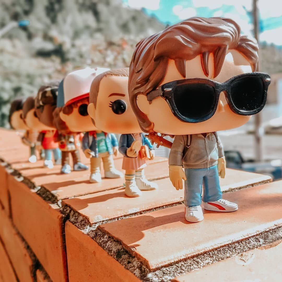 Funko Pop 奇異博士 壁紙 — 一排來自《怪奇物語》的 Funko Pop 人偶站在陽光普照的磚牆上，背景是岩石山坡。