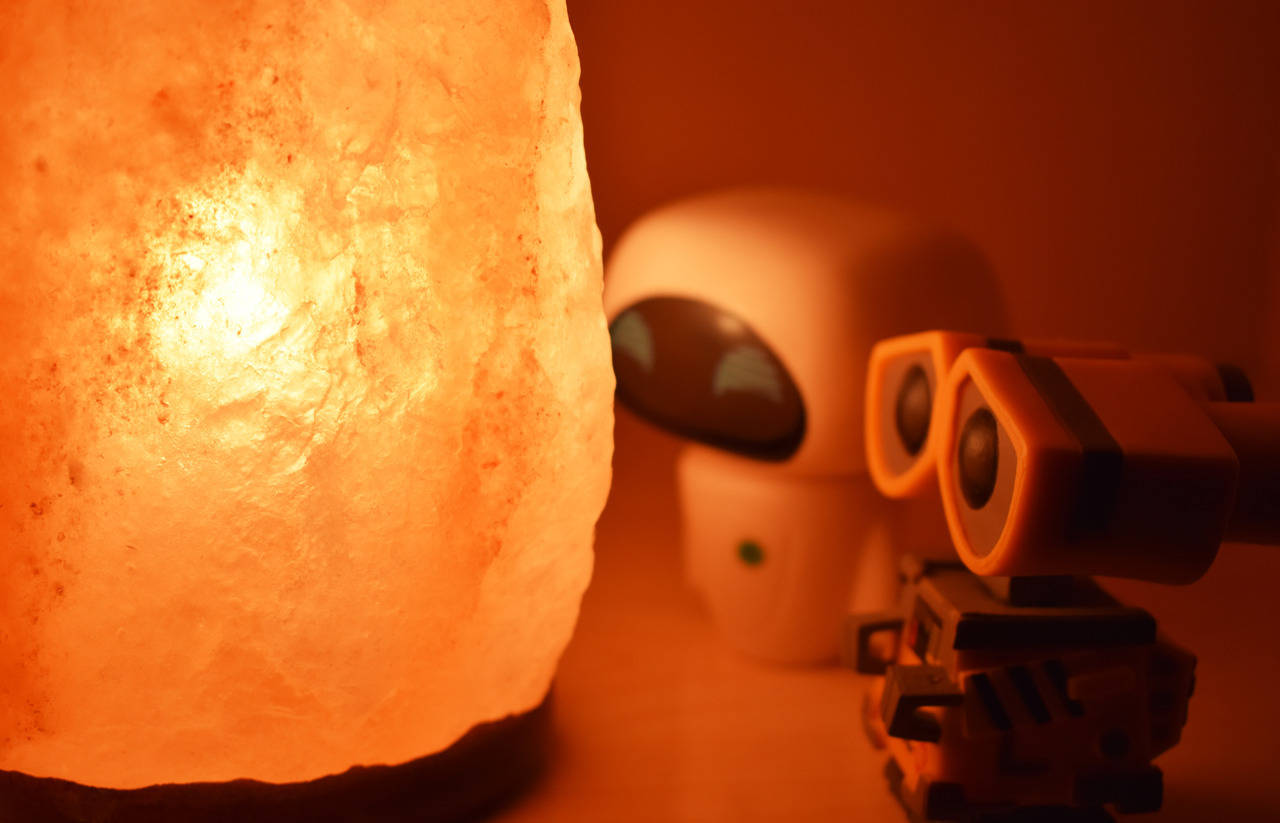 Funko Pop WALL-E 與 EVE 壁紙 — 一個發光的橙色鹽燈，旁邊有兩個小型機械人公仔，讓房間沐浴在溫暖的光線中。
