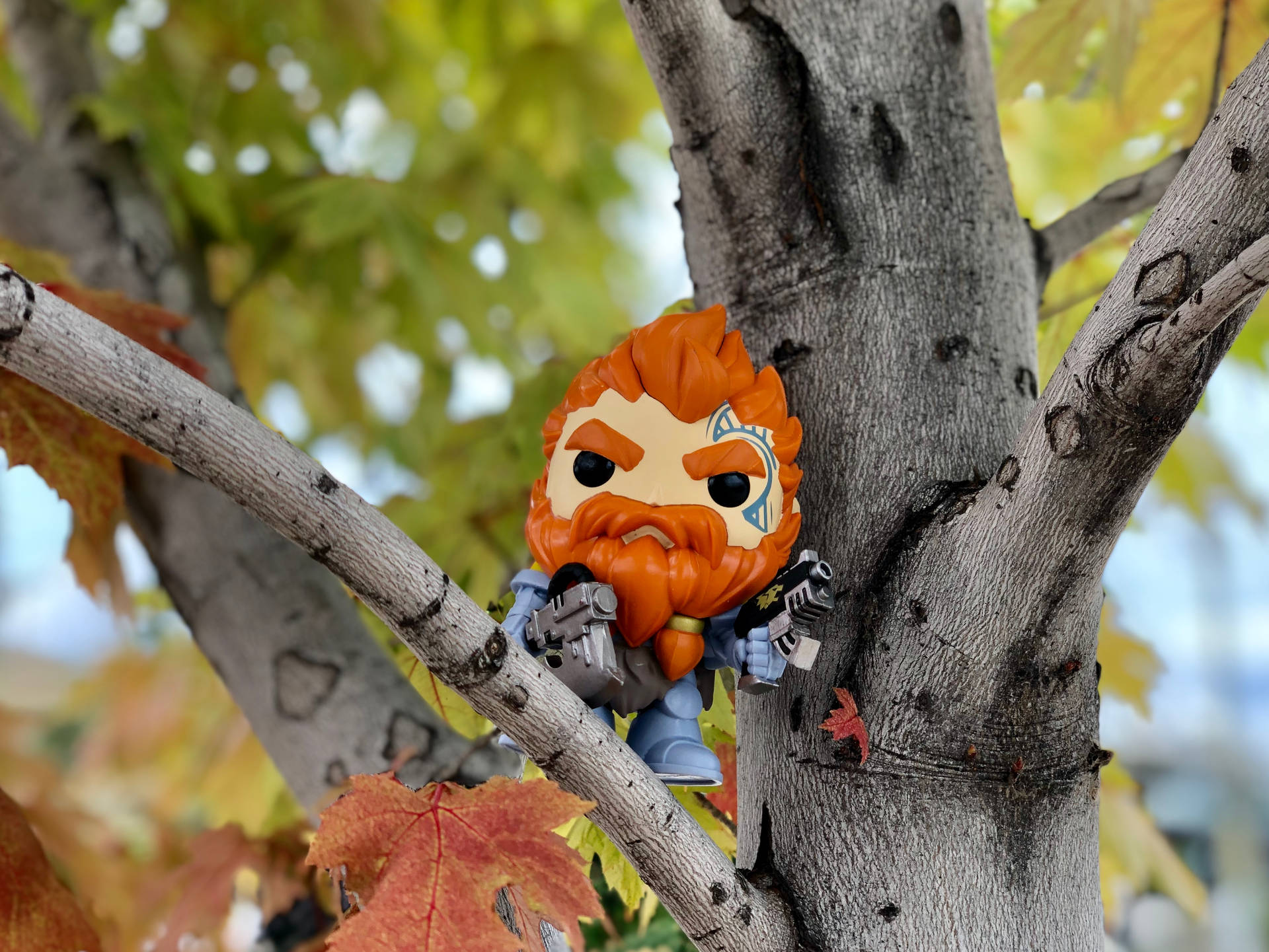 橙色頭髮和鬍子的Funko Pop公仔棲息在樹枝上，伴有秋葉。
