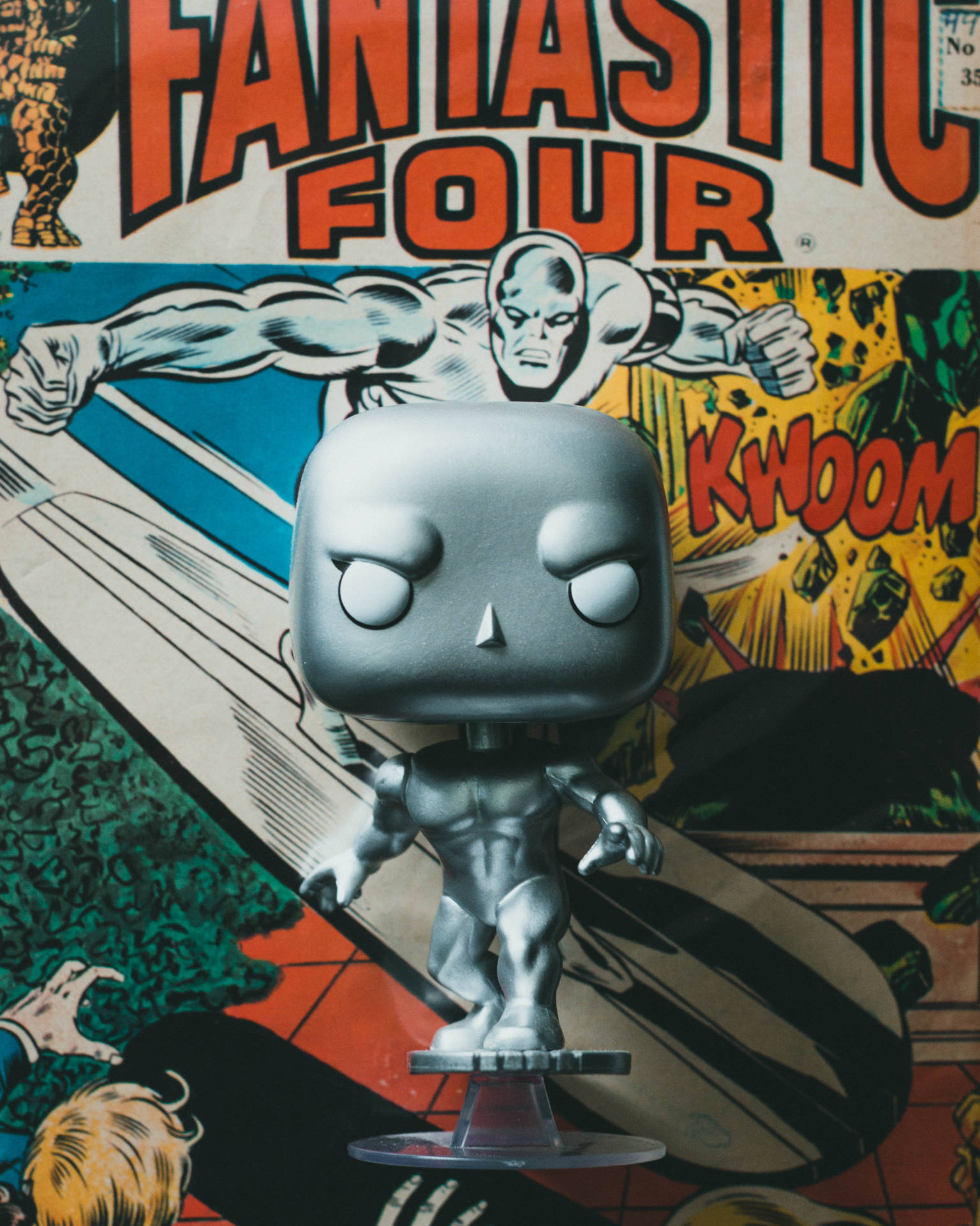 銀色滑翔者Funko Pop！人偶放在透明支架上，背景是神奇四俠漫畫封面。