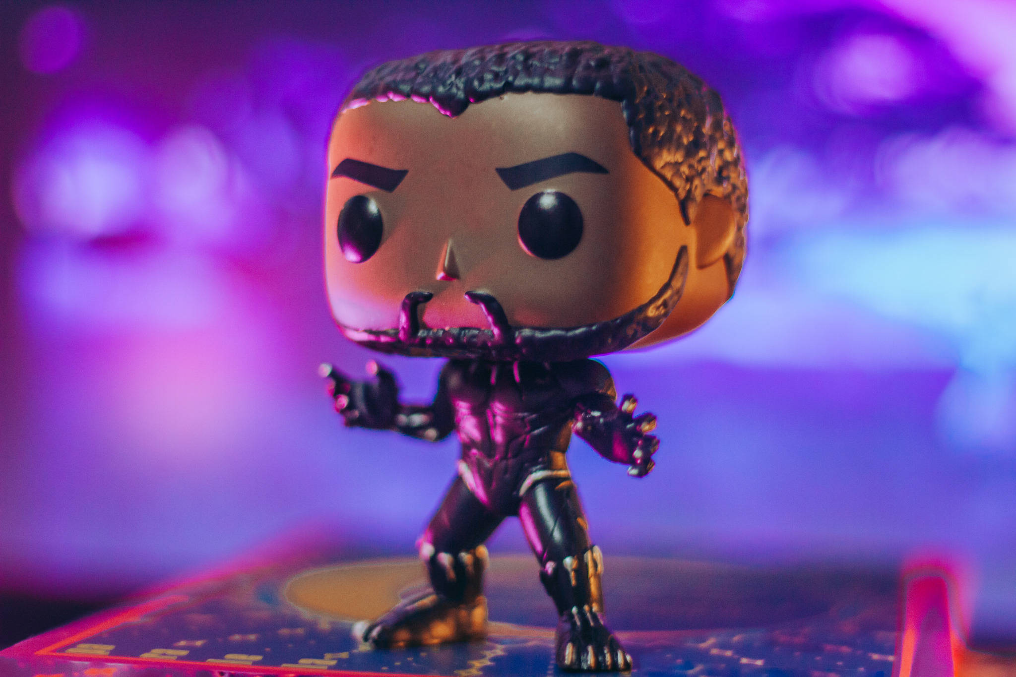 Funko Pop 黑豹 壁紙 — 一個 Funko Pop 黑豹人偶在充滿活力的紫色和藍色散景背景前擺好姿勢。