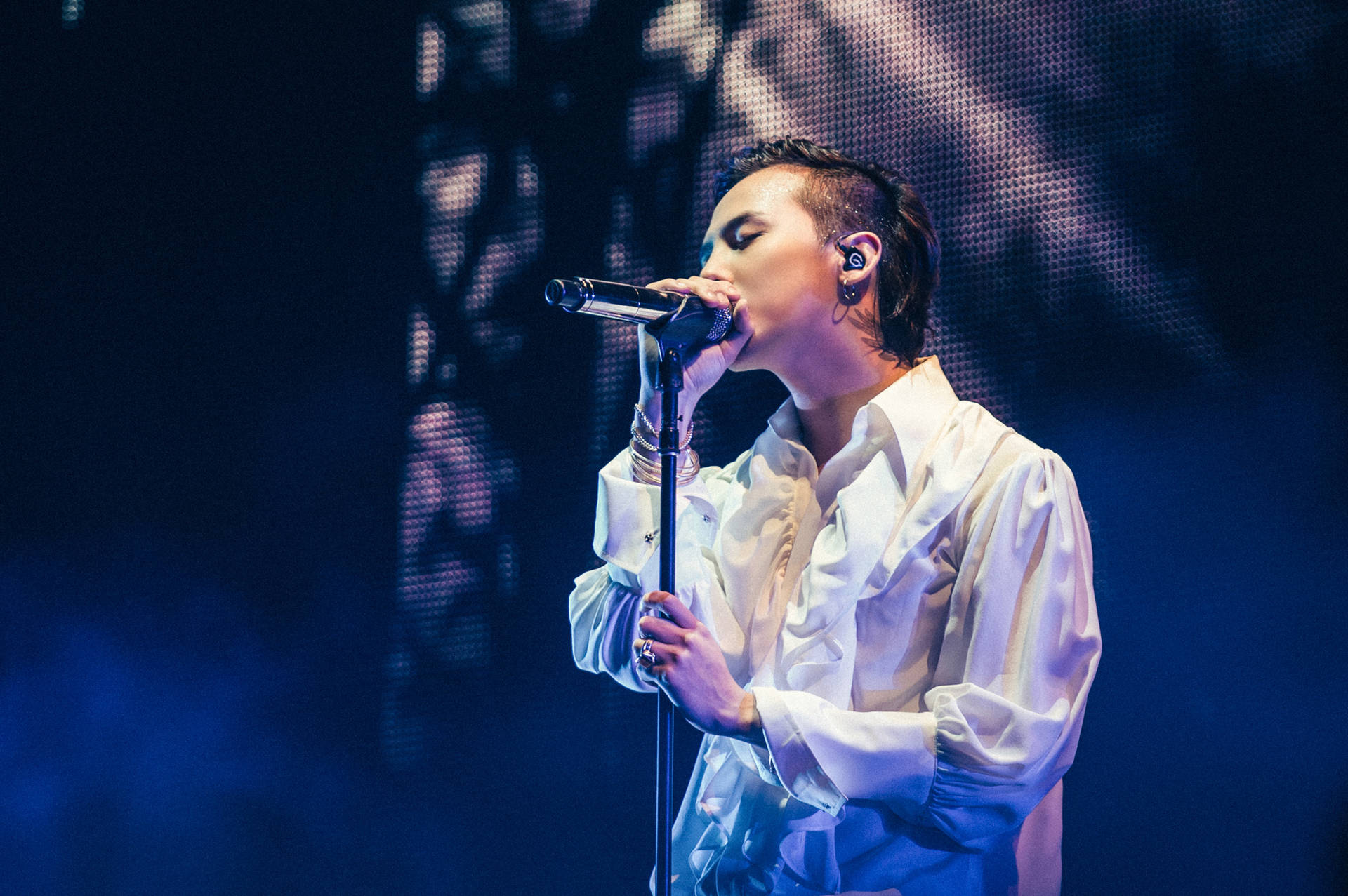 男歌手在藍光下身穿白恤衫在舞台上表演。