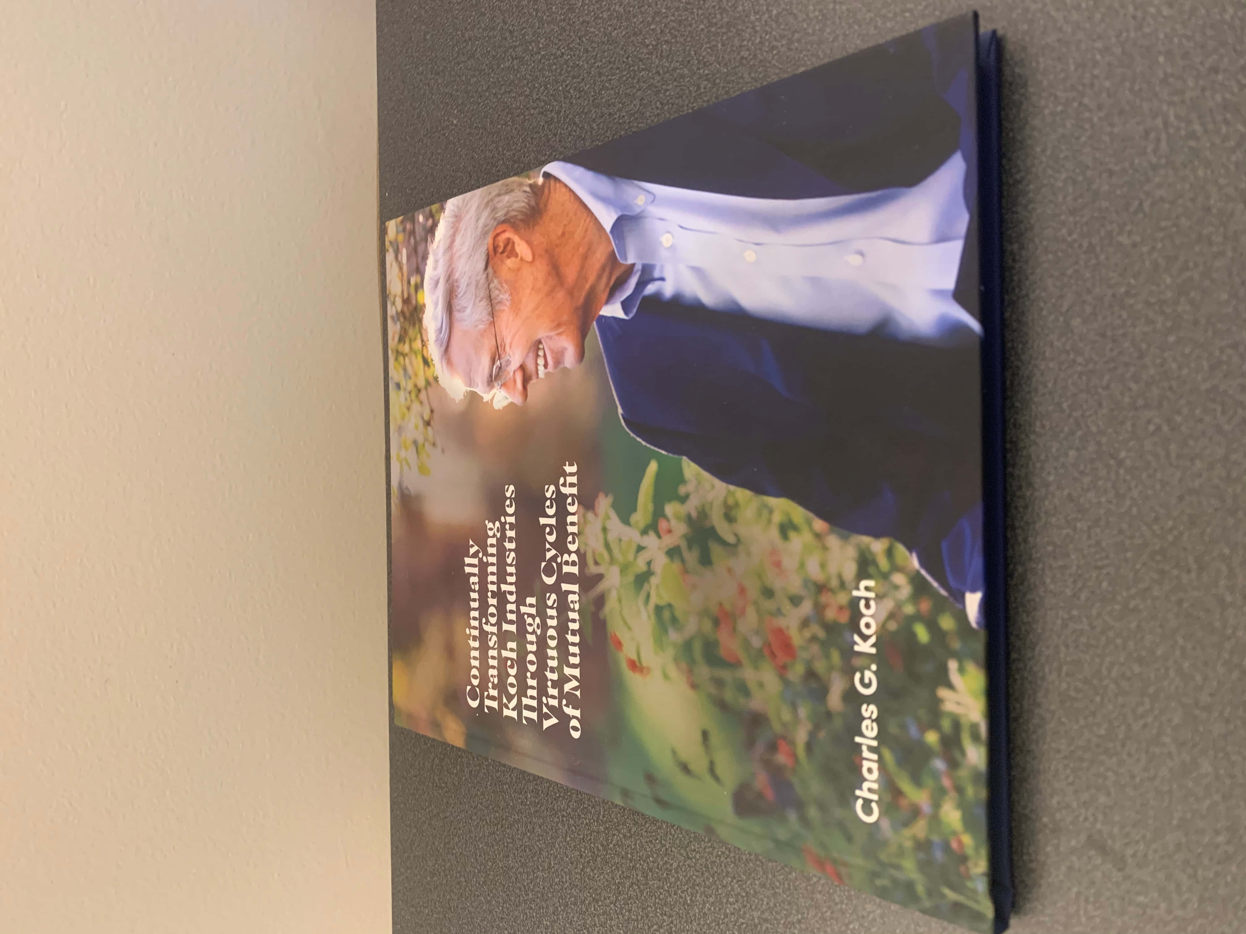 查爾斯·G·科赫肖像照 壁紙 — 一本由Charles G. Koch撰寫的書《Continually Improving Koch Industries Through Virtuous Cycles of Mutual Benefit》斜放在灰色表面上。