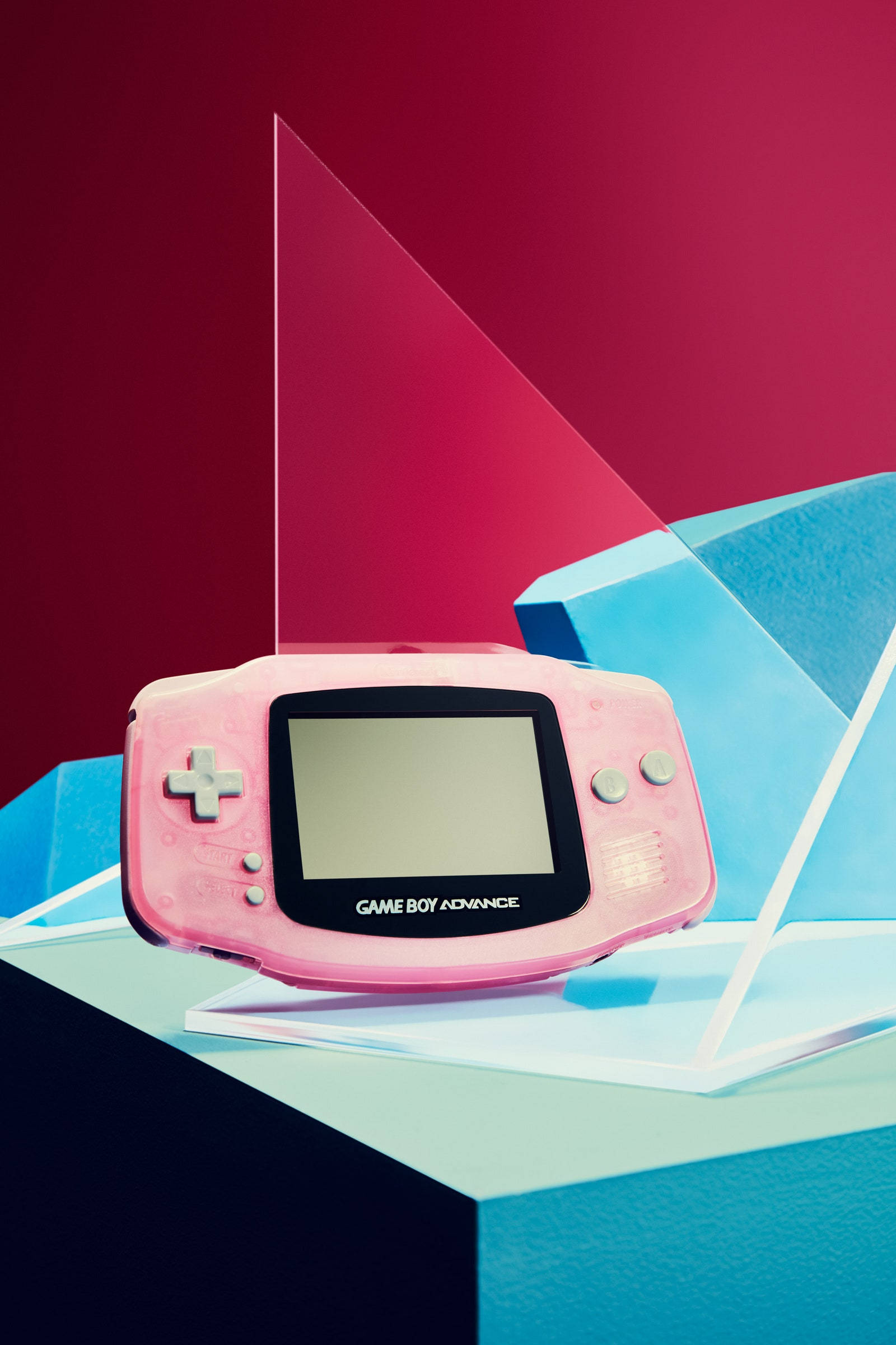 Game Boy Advance 立於藍色平台 壁紙 — 一部粉紅色 Game Boy Advance 放置在幾何藍色和黑色方塊上，背景為大膽的紅色。