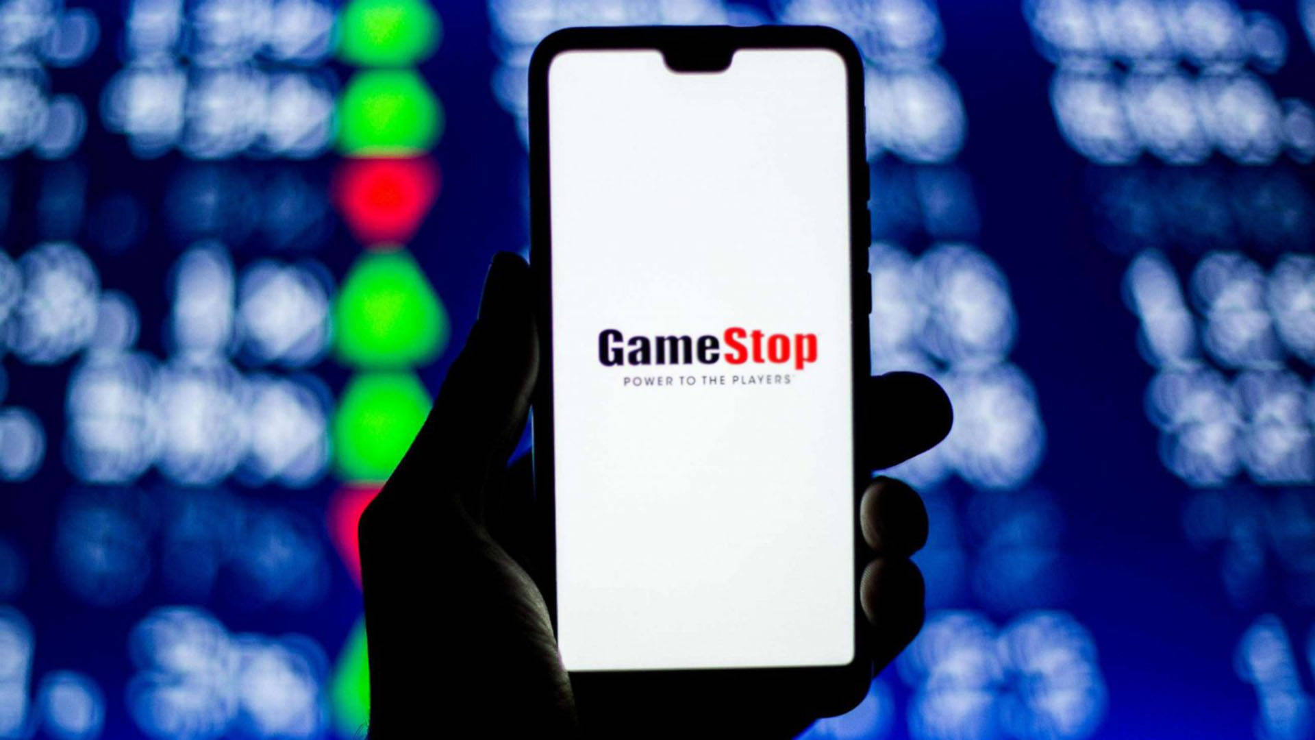 GameStop手機螢幕插畫 壁紙 — 一隻手拿著智能手機，顯示GameStop標誌，背景是模糊的股票市場行情燈光。