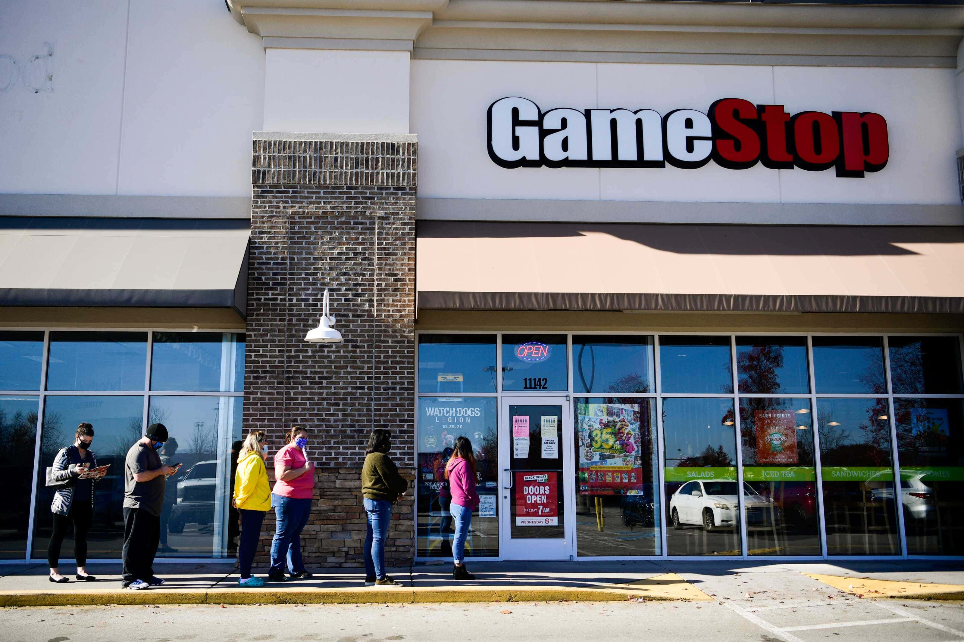 成為遊戲中的主角，與GameStop一起玩！ 壁紙 — 人們在明亮的日光下於 GameStop 商店外排隊，玻璃窗上有清晰的倒影。