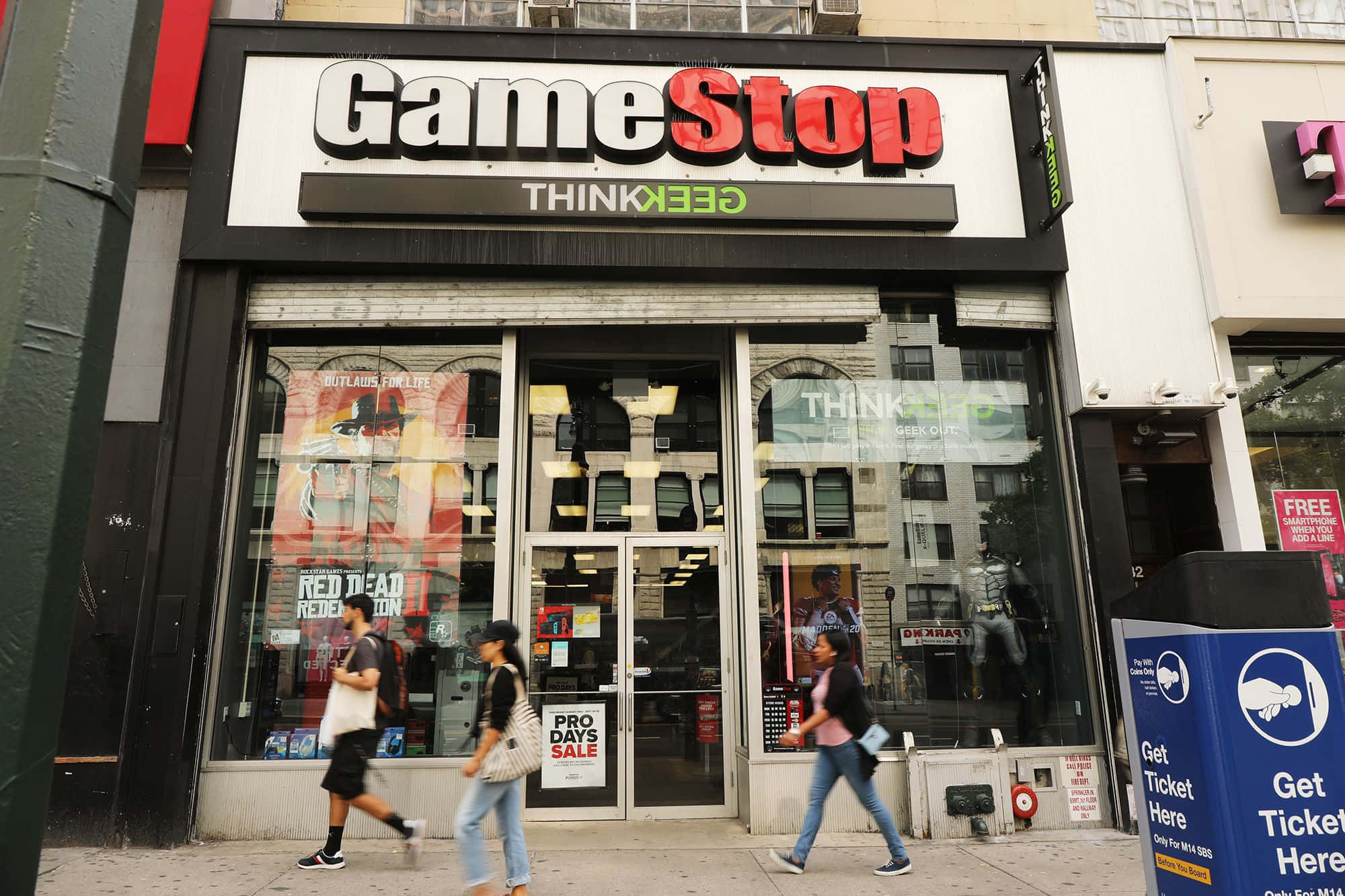 於Gamestop搶購最新遊戲 壁紙 — 行人經過一間GameStop店舖，玻璃窗內可見醒目的招牌和遊戲海報。