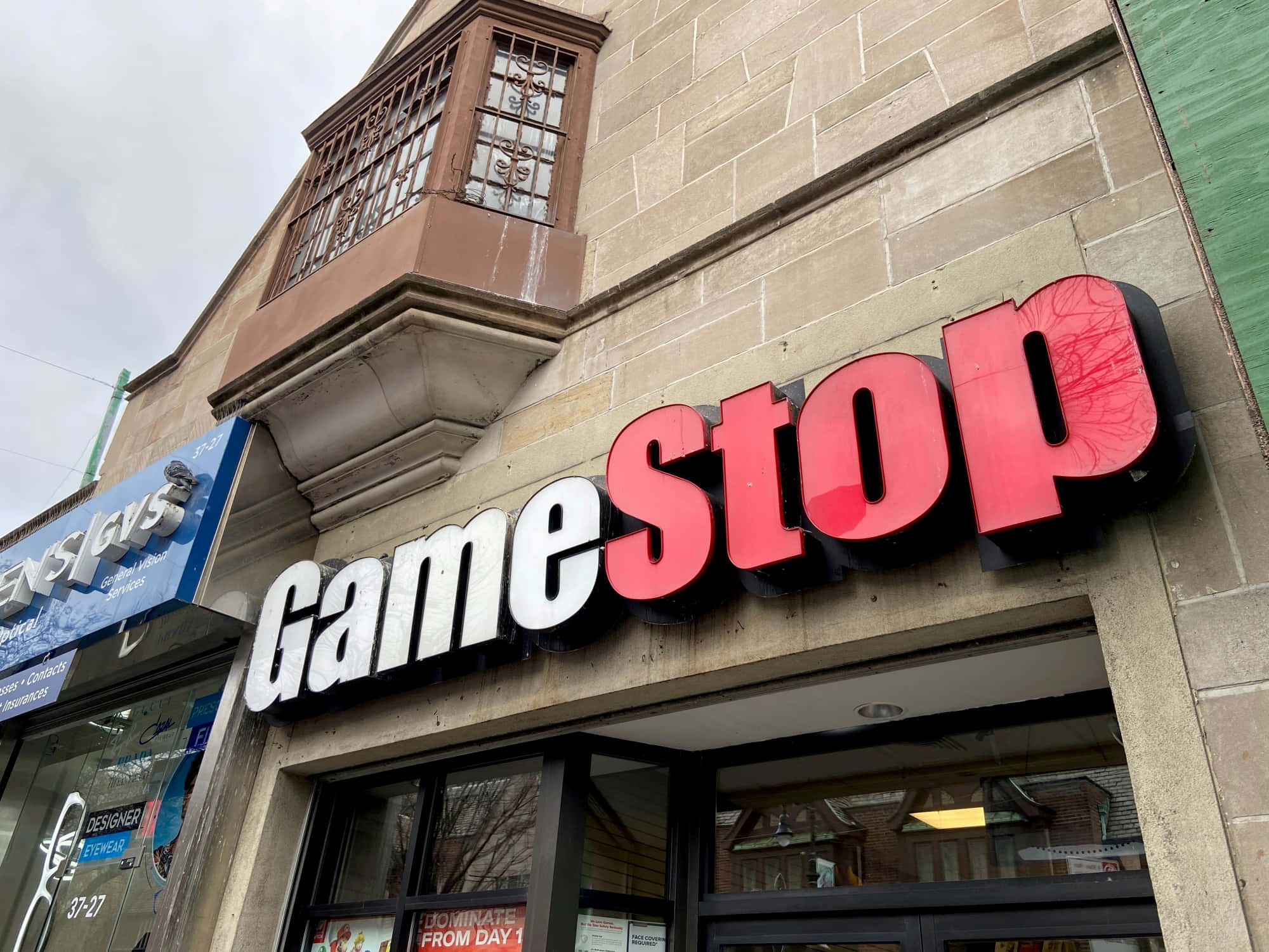 於Gamestop提升你的遊戲體驗 壁紙 — 一張低角度拍攝的GameStop店面照片，在陰天背景下，石造建築上裝有醒目的紅白招牌。