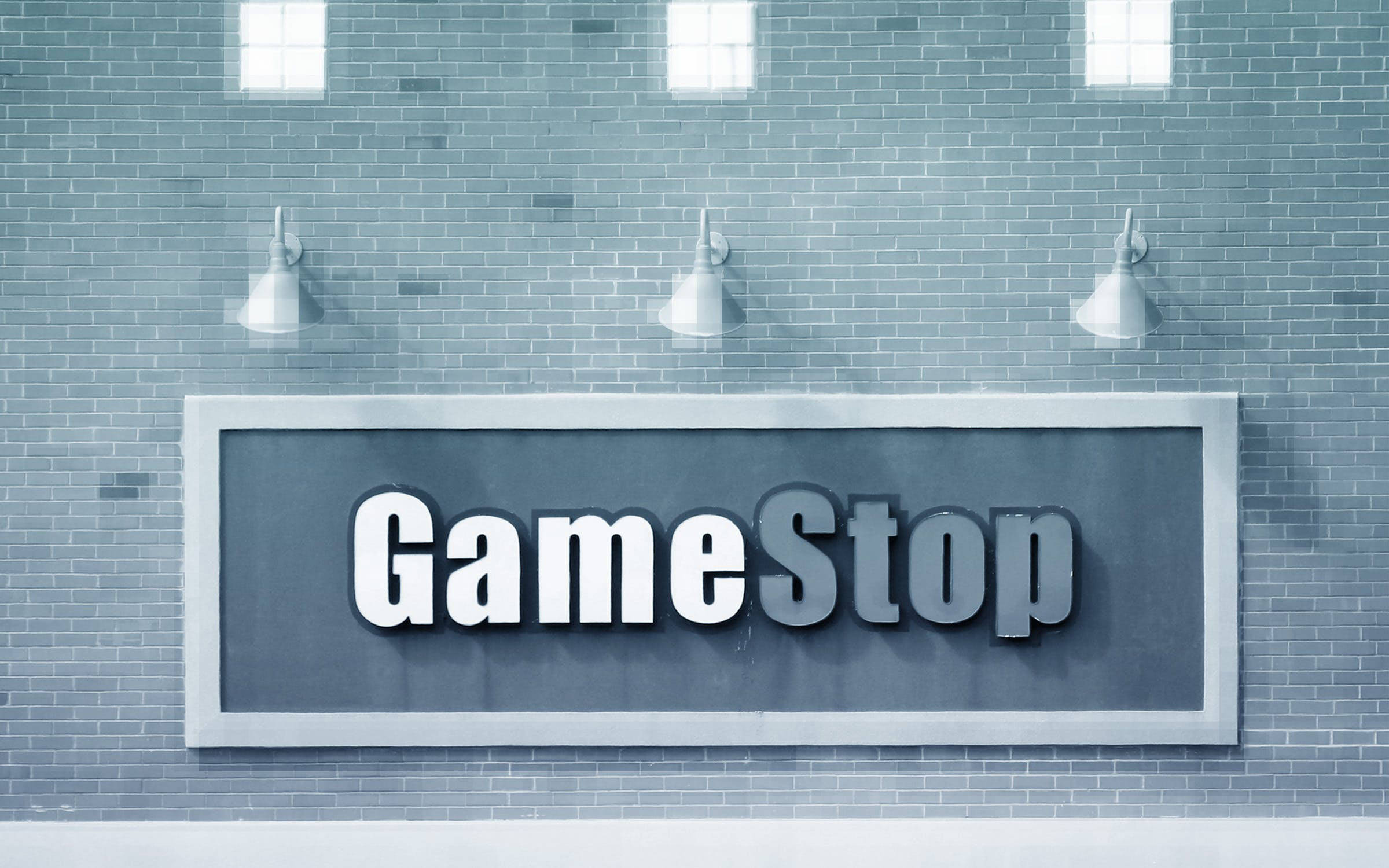 GameStop 灰色磚牆壁紙 壁紙 — 一個大型GameStop標誌安裝在灰色磚牆上，下方有三盞工業風格的燈。