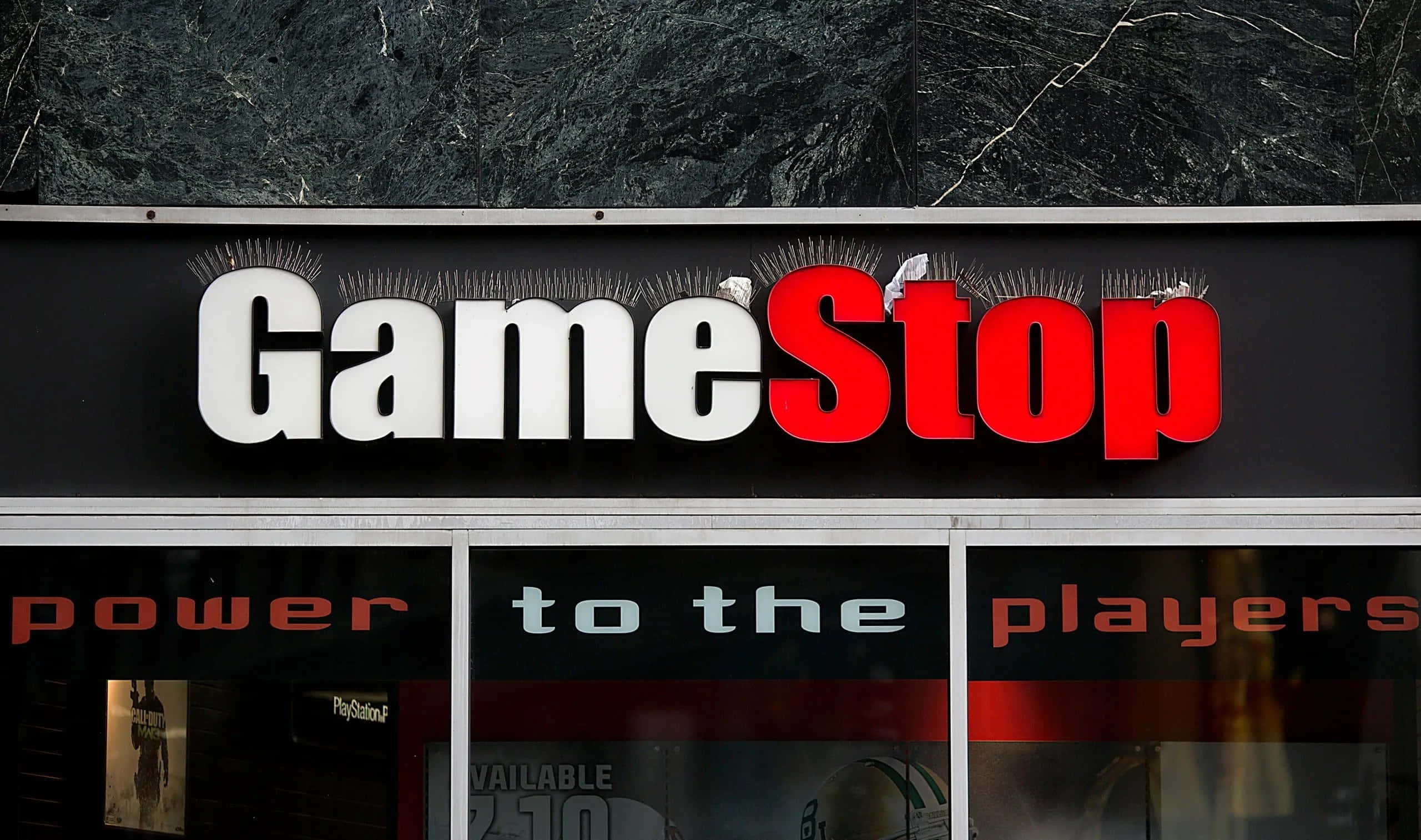 Gamestop - 購買最新熱門遊戲！ 壁紙 — GameStop 店舖招牌，以粗體紅白字體安裝在深色大理石外牆上。