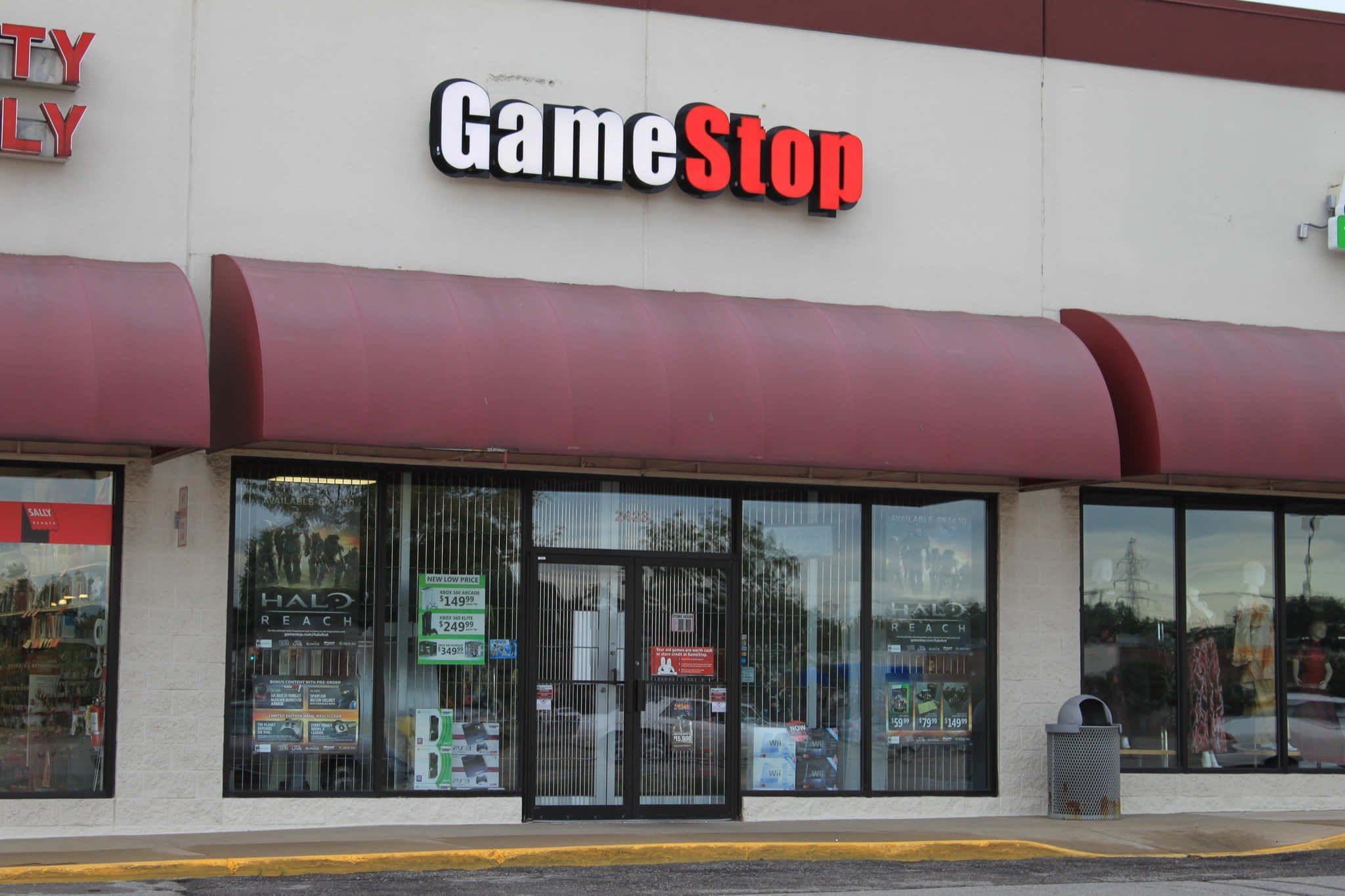 GameStop：重玩的終極目的地 壁紙 — GameStop 店舖正面，紅色簷篷和玻璃門展示 Halo Reach 海報和價格標籤。