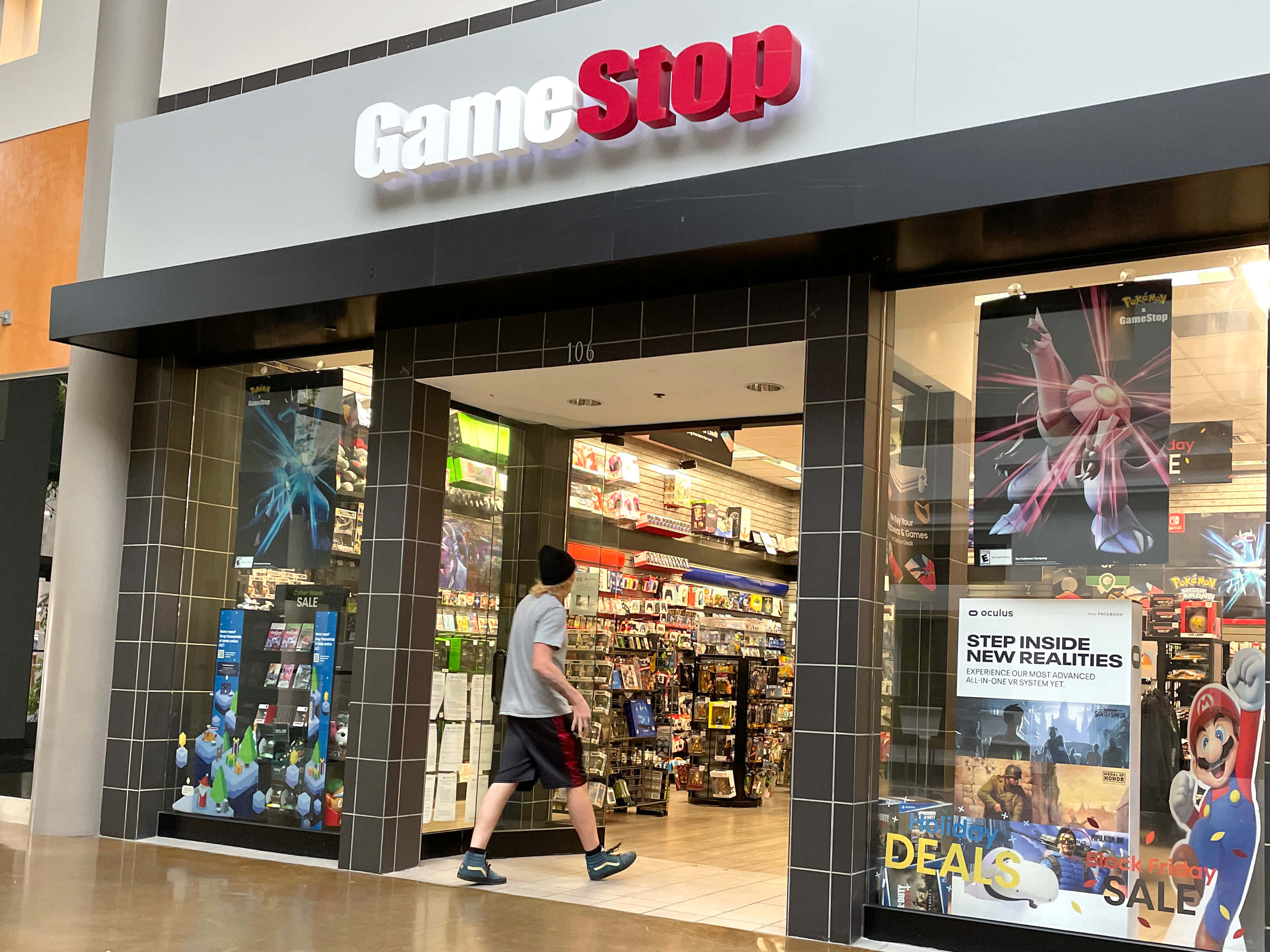 GameStop現有最新PS5遊戲 壁紙 — 一個人走過商場內燈光明亮的GameStop店舖，展示著電子遊戲海報和商品。