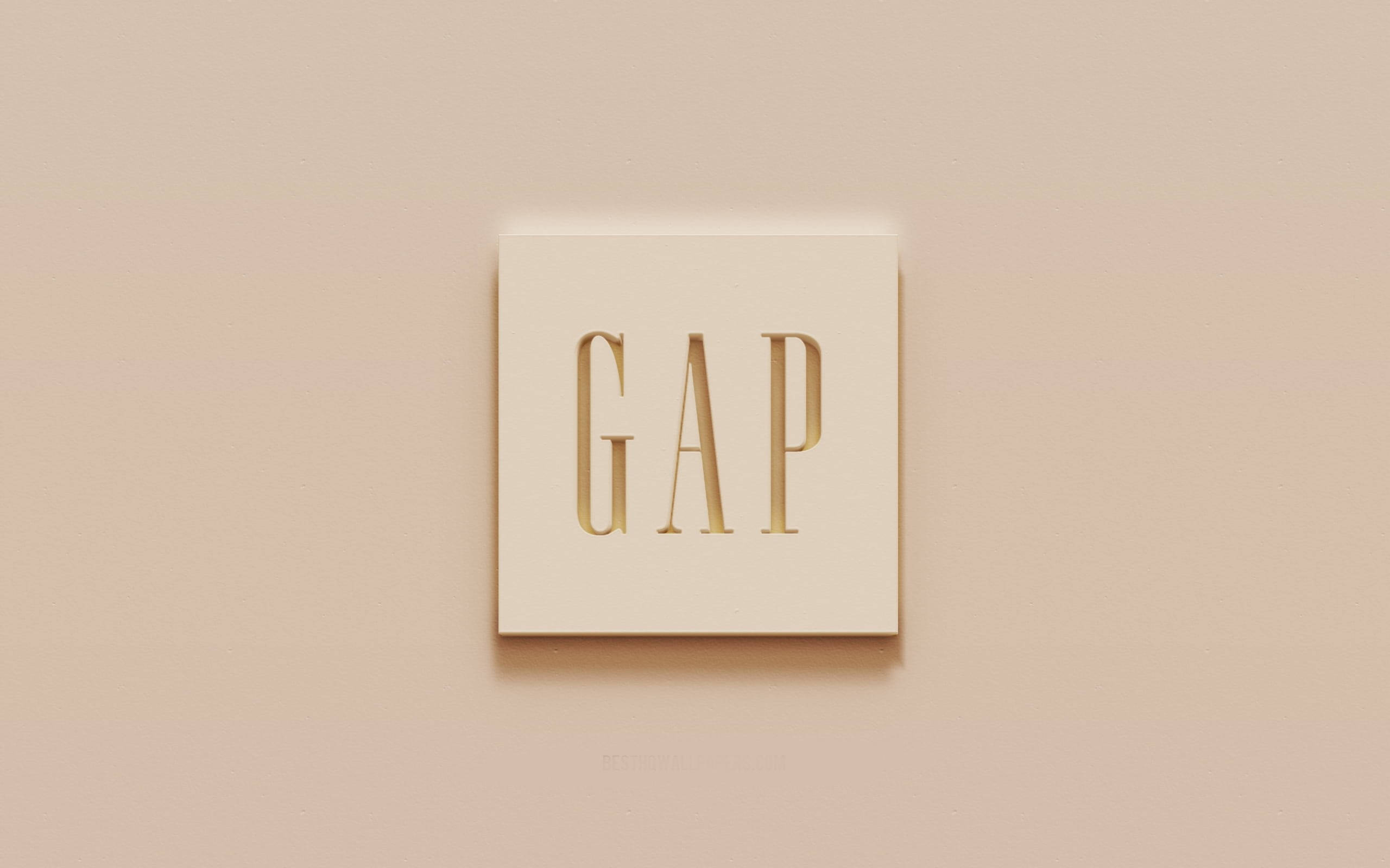 Gap 的淡粉紅色標誌美學 壁紙 — 簡約米色牆上有一個方形奶油色牌匾，帶有金色壓花GAP標誌，投射出柔和陰影。