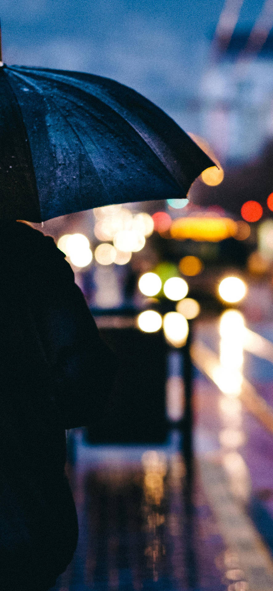 拿著黑色雨傘的人在雨夜的城市中行走，燈光閃爍。