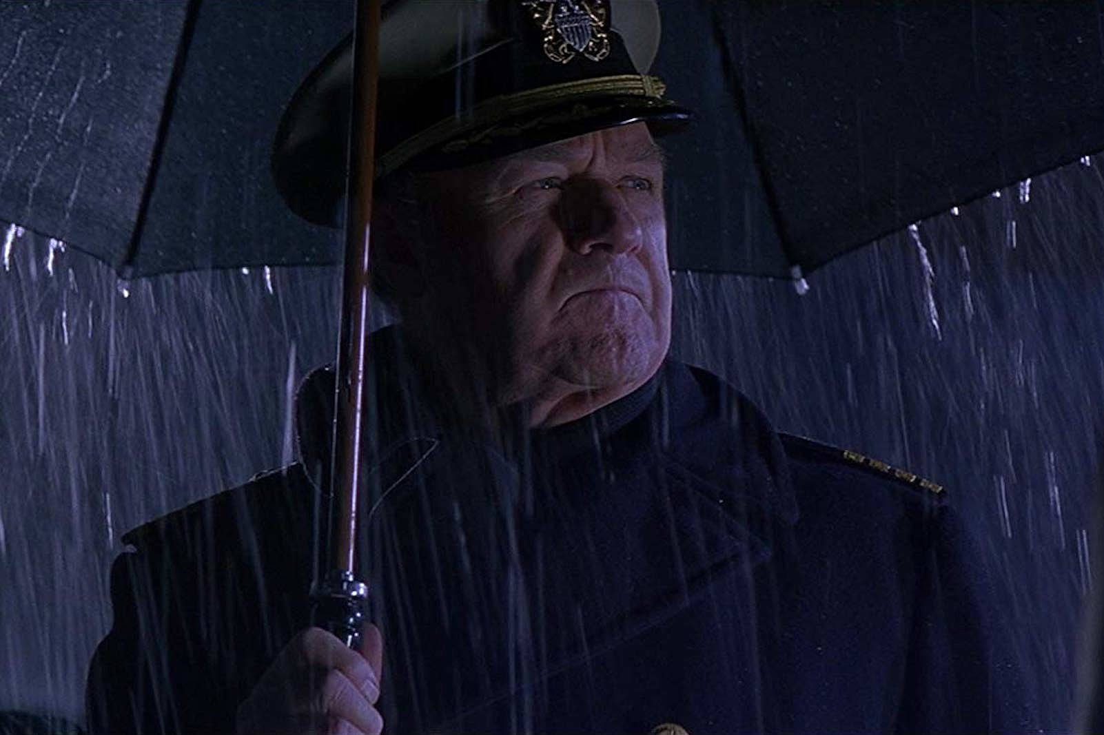 一位海軍軍官在藍色燈光下的大雨中撐著雨傘。