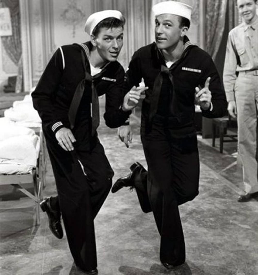 Gene Kelly 黑白照片 壁紙 — 兩名身穿制服的水手帶著頑皮的表情精力充沛地跑過醫院病房。