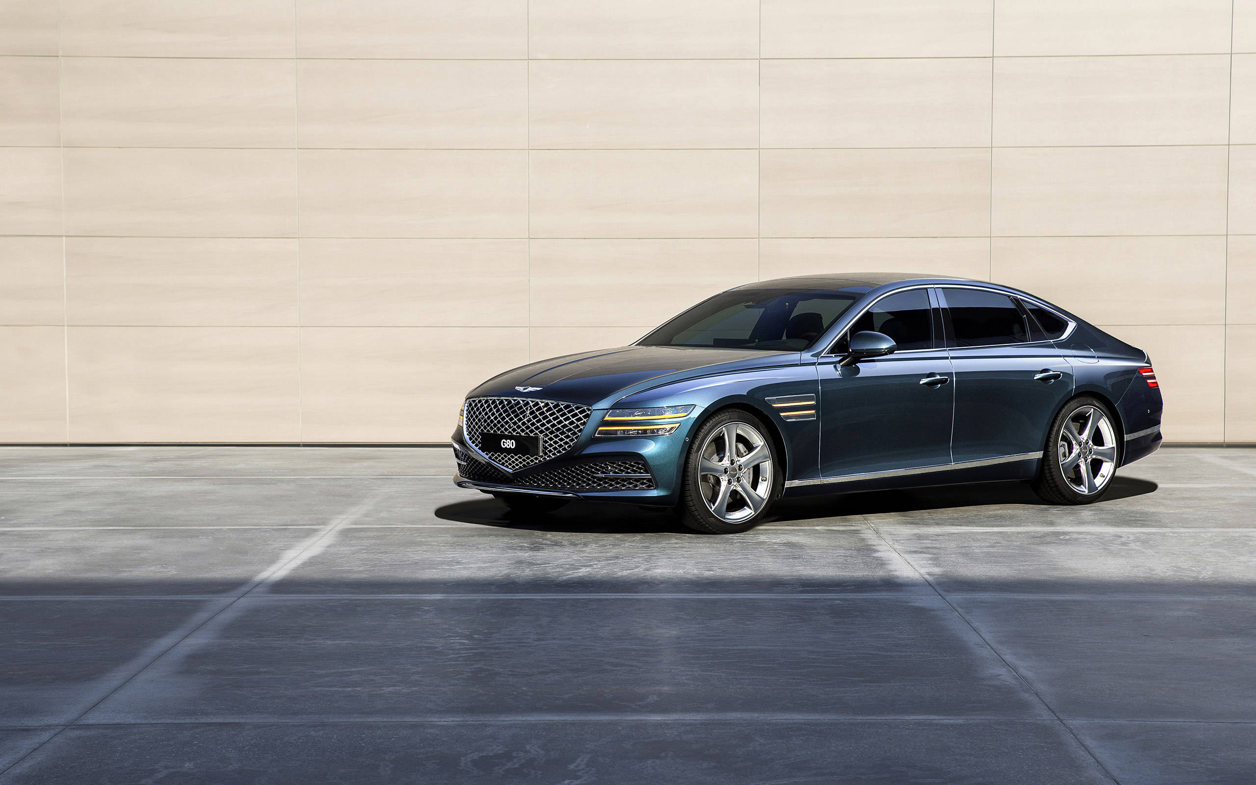 森林綠色 Genesis G80 壁紙 — 一輛時尚的藍色Genesis G90豪華轎車停在混凝土上，背景是簡約的米色牆壁，在明亮的日光下。