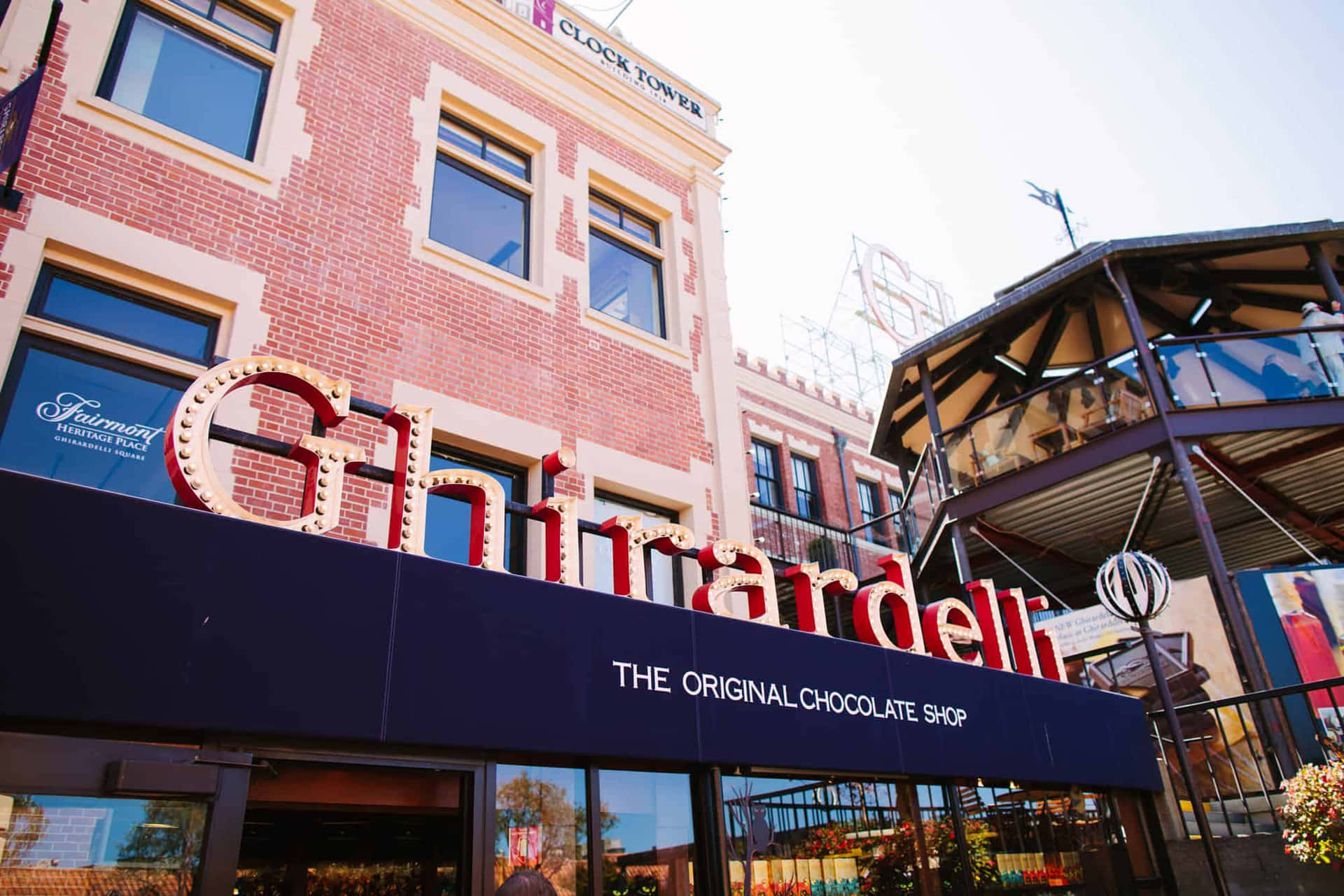 磚造建築上嘅 Ghirardelli 朱古力店招牌，背景有摩天輪同鐘樓。