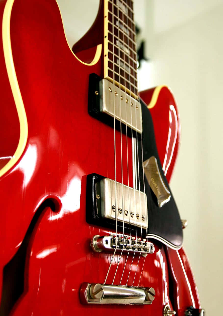 亮面紅色Gibson 335 壁紙 — 在柔和白色背景上，帶有金色飾邊和鍍鉻硬件的亮紅色電結他的特寫。