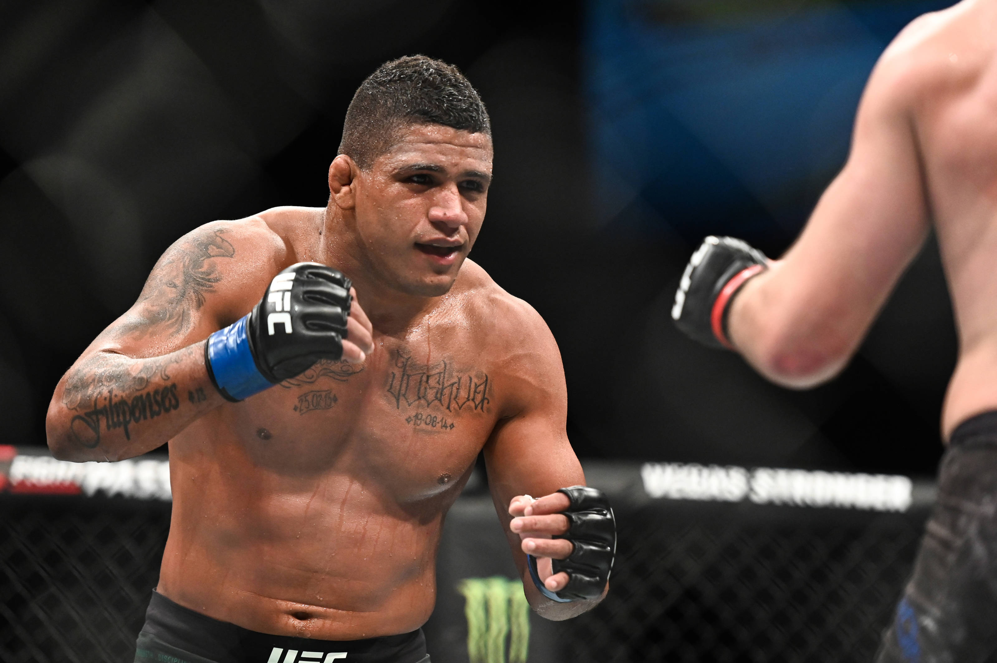 Gilbert Burns 擊拳準備 壁紙 — 一位肌肉發達、帶有紋身和UFC手套的拳手在八角籠內的混合武術比賽中凝視著對手。