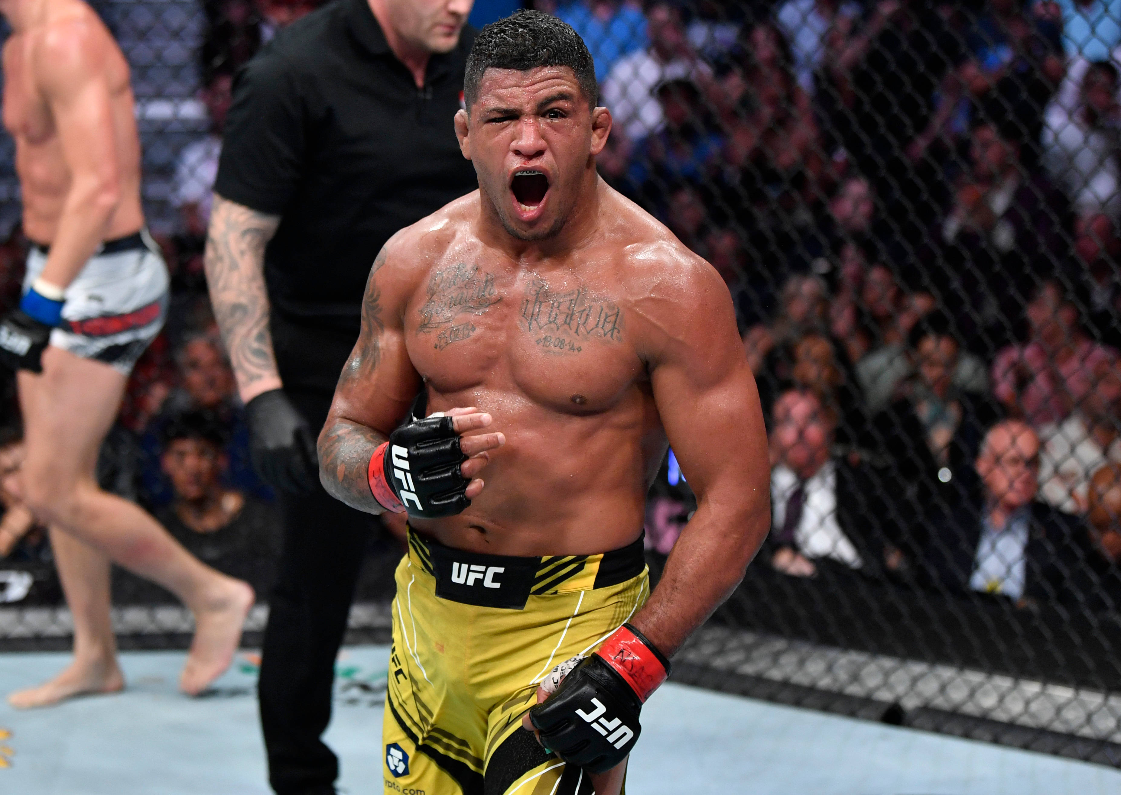 Gilbert Burns 賽前激勵 壁紙 — 一位肌肉發達的UFC拳手在八角籠內勝利咆哮，背景有粉絲歡呼。