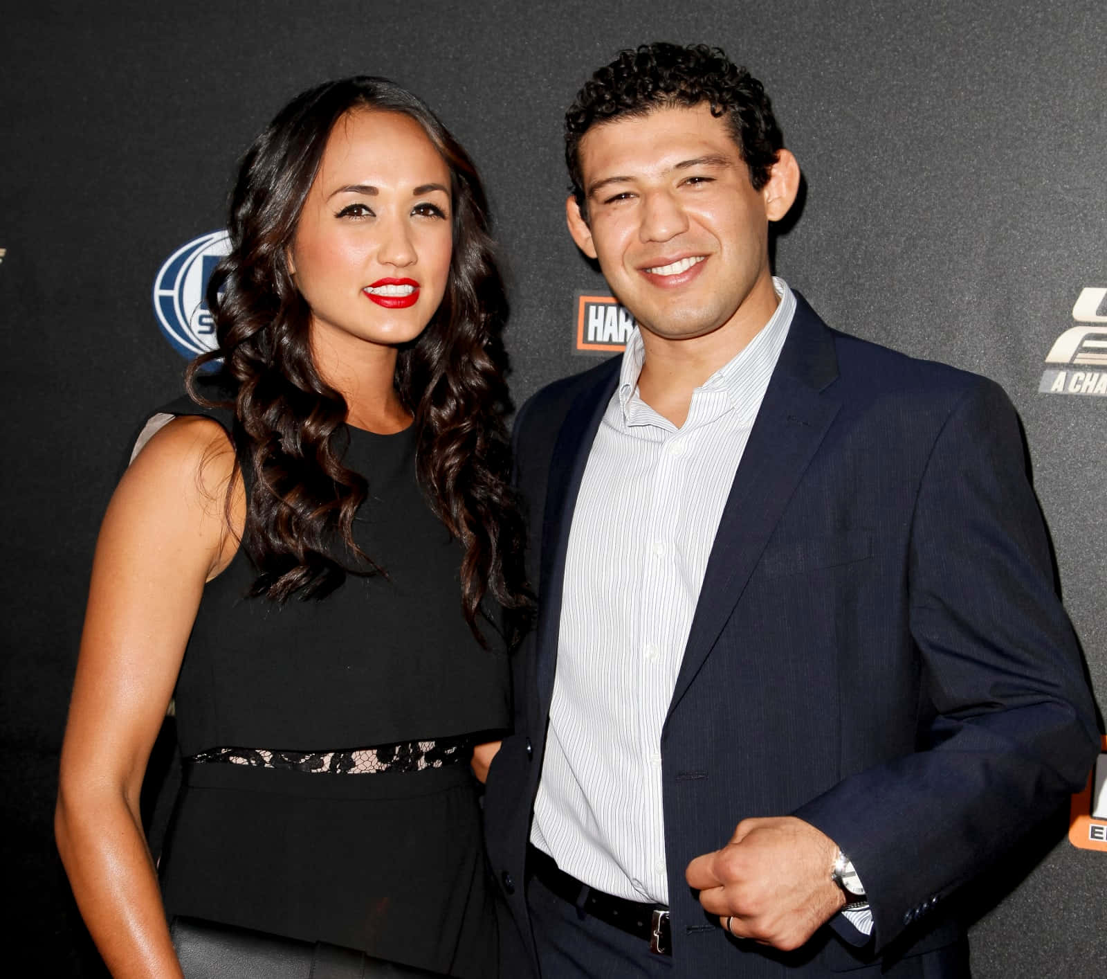 Gilbert Melendez與妻子出席《The Ultimate Fighter》首映派對 壁紙 — 一位微笑的男士和女士在品牌背景前於正式活動中一起擺姿勢。
