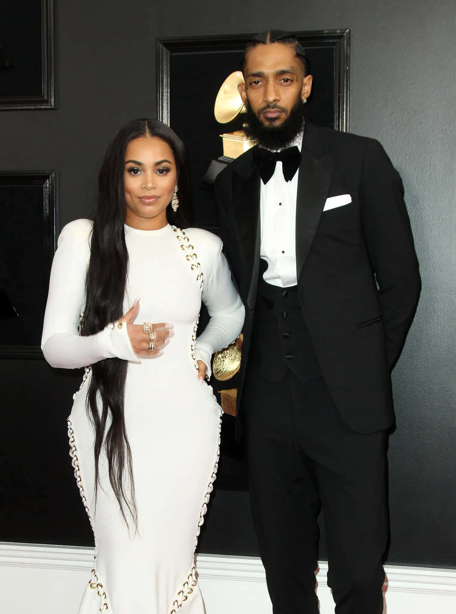 Lauren London 桌布 壁紙 — 一對魅力情侶穿著正式服裝，在深色牆壁前擺姿勢，身後有格林美獎獎座。