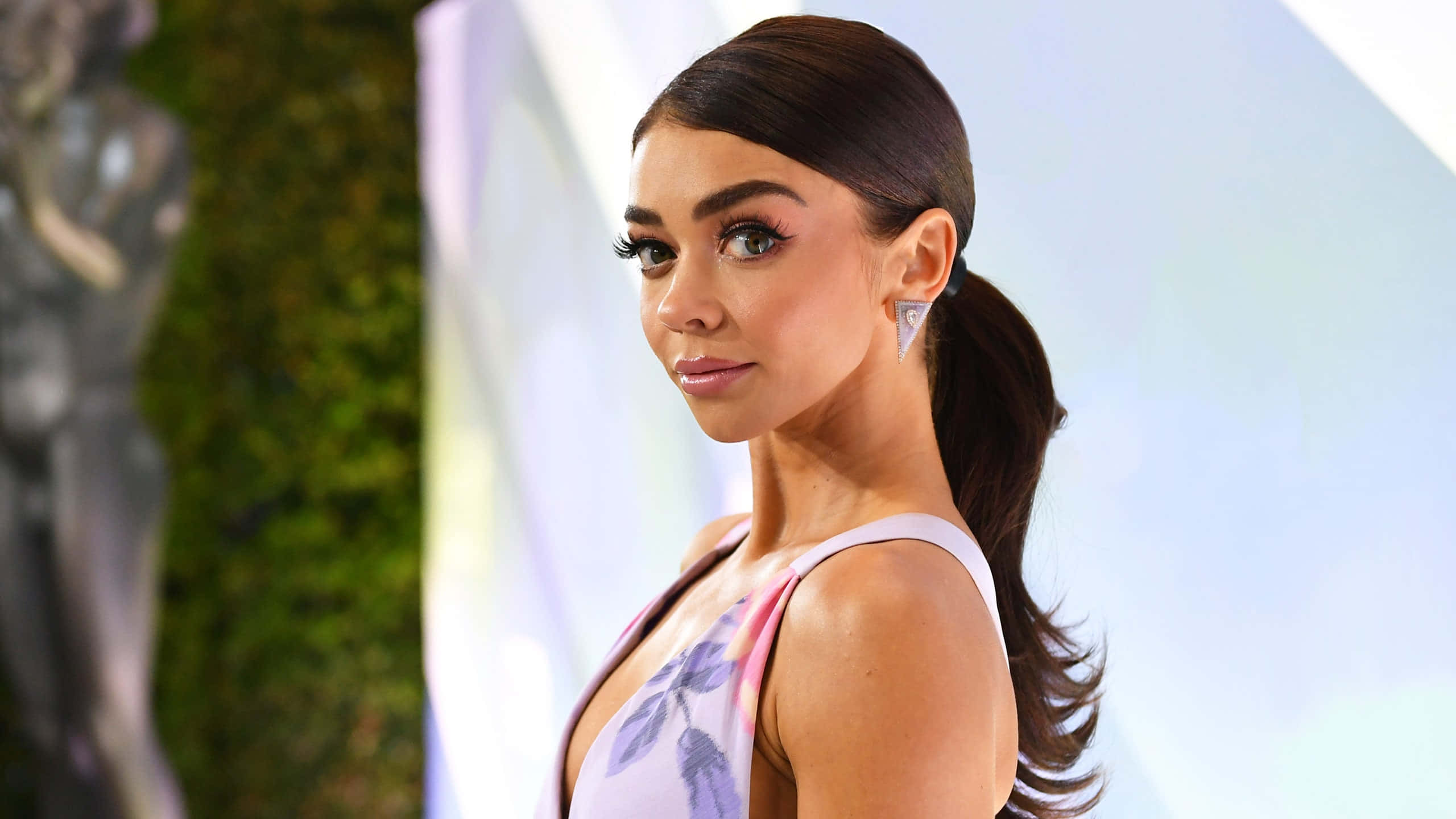 Sarah Hyland 桌布 壁紙 — 一位魅力四射的深色頭髮馬尾辮女性，在紅地毯活動中穿著花卉連衣裙和鑽石耳環。