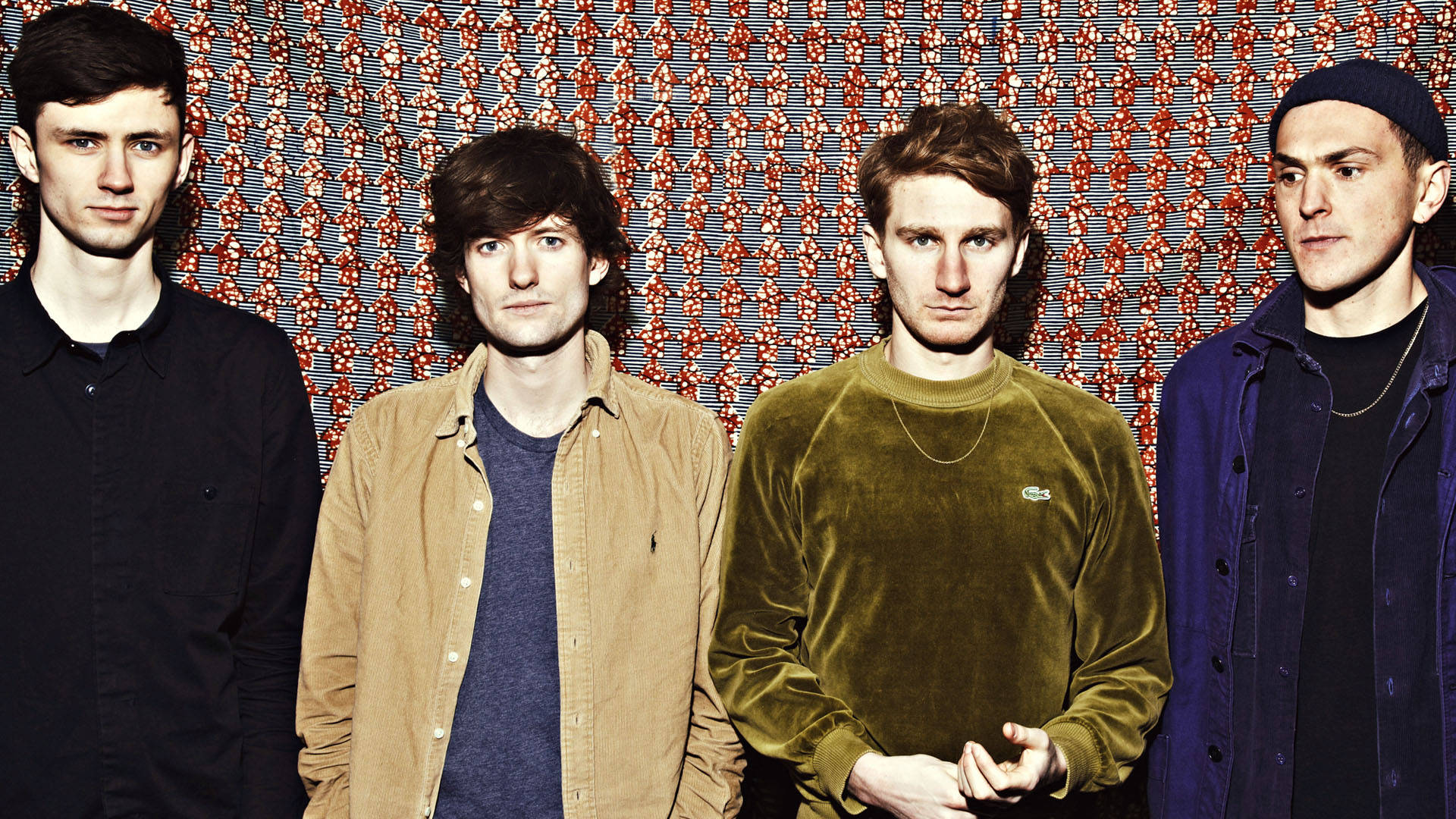 Glass Animals 創團時期經典影像 壁紙 — 四個穿著休閒服的男人站在有紋理的紅灰圖案牆前，表情嚴肅。