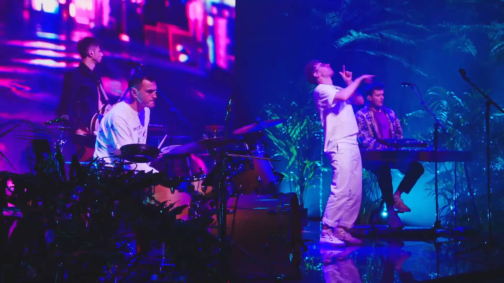 Glass Animals 演唱會 壁紙 — 樂隊在充滿活力的紫色和藍色舞台燈光下表演，背景有熱帶植物。
