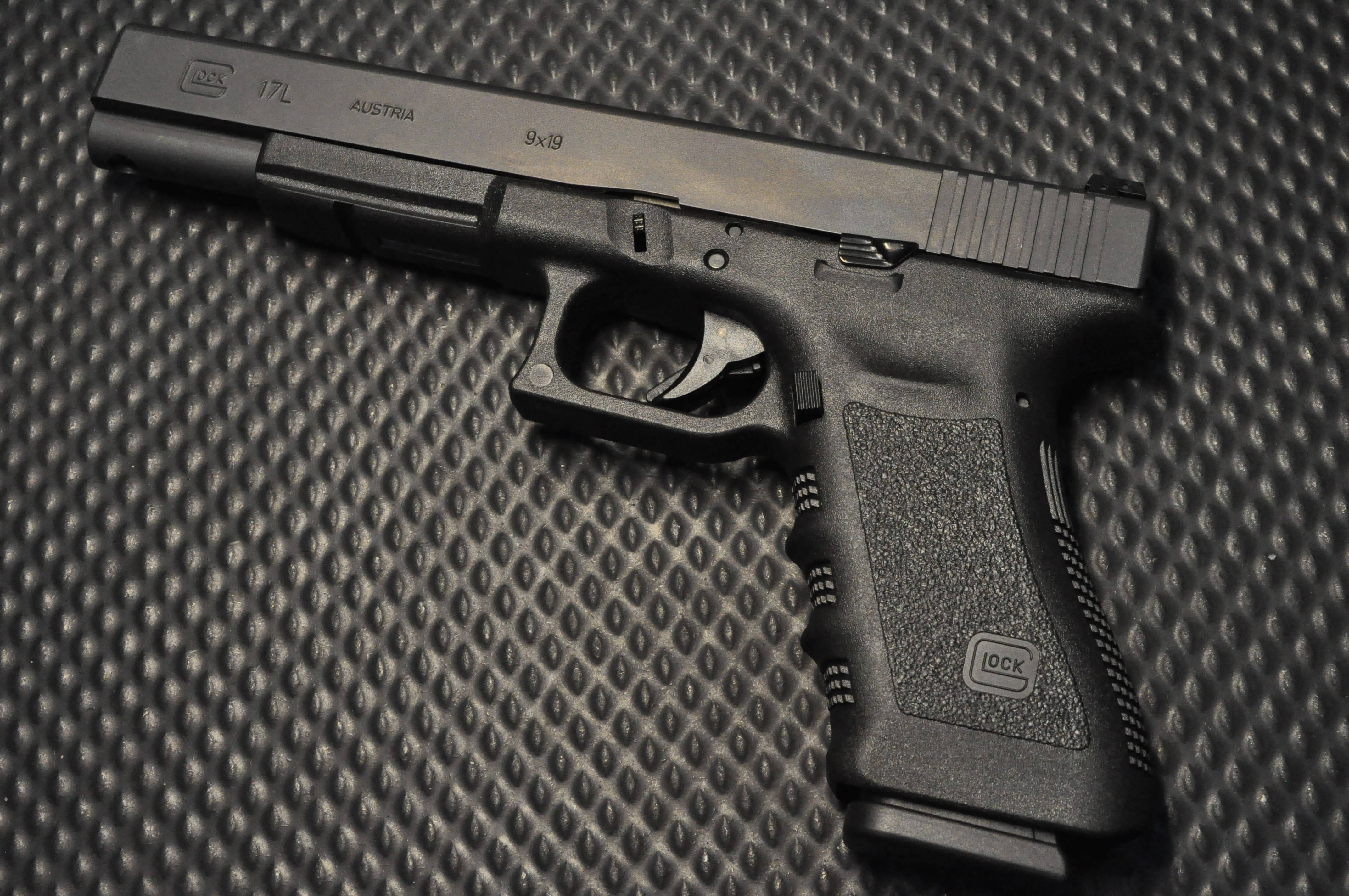 Glock 17L 置於金屬表面 壁紙 — 一把黑色Glock 17L手槍放置在帶紋理的黑色表面上，精確的燈光凸顯其輪廓和雕刻。