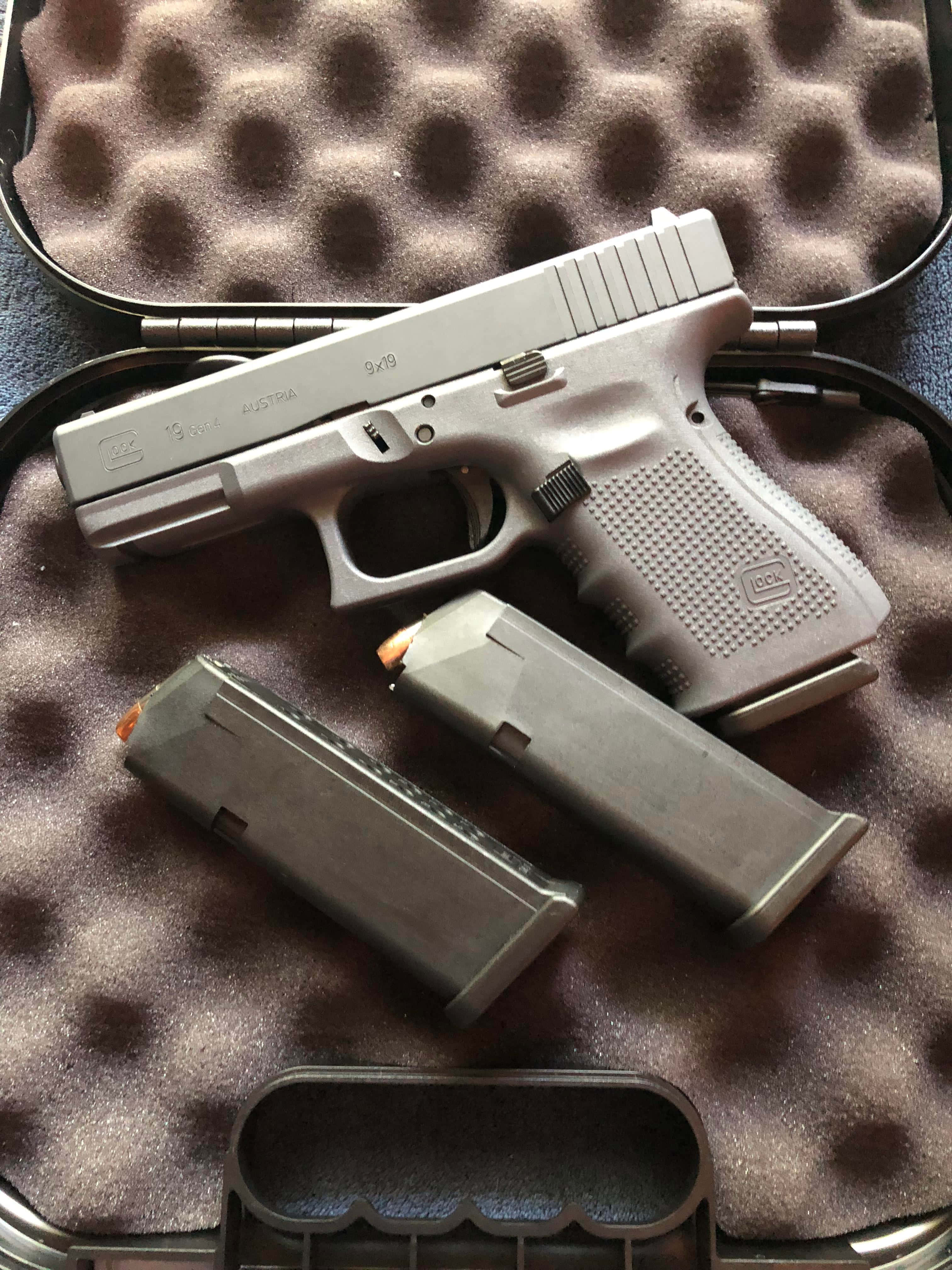 Glock 19 半自動手槍 壁紙 — 一把銀色Glock手槍連同兩個彈匣，在明亮燈光下放置於泡棉內襯的盒子中。