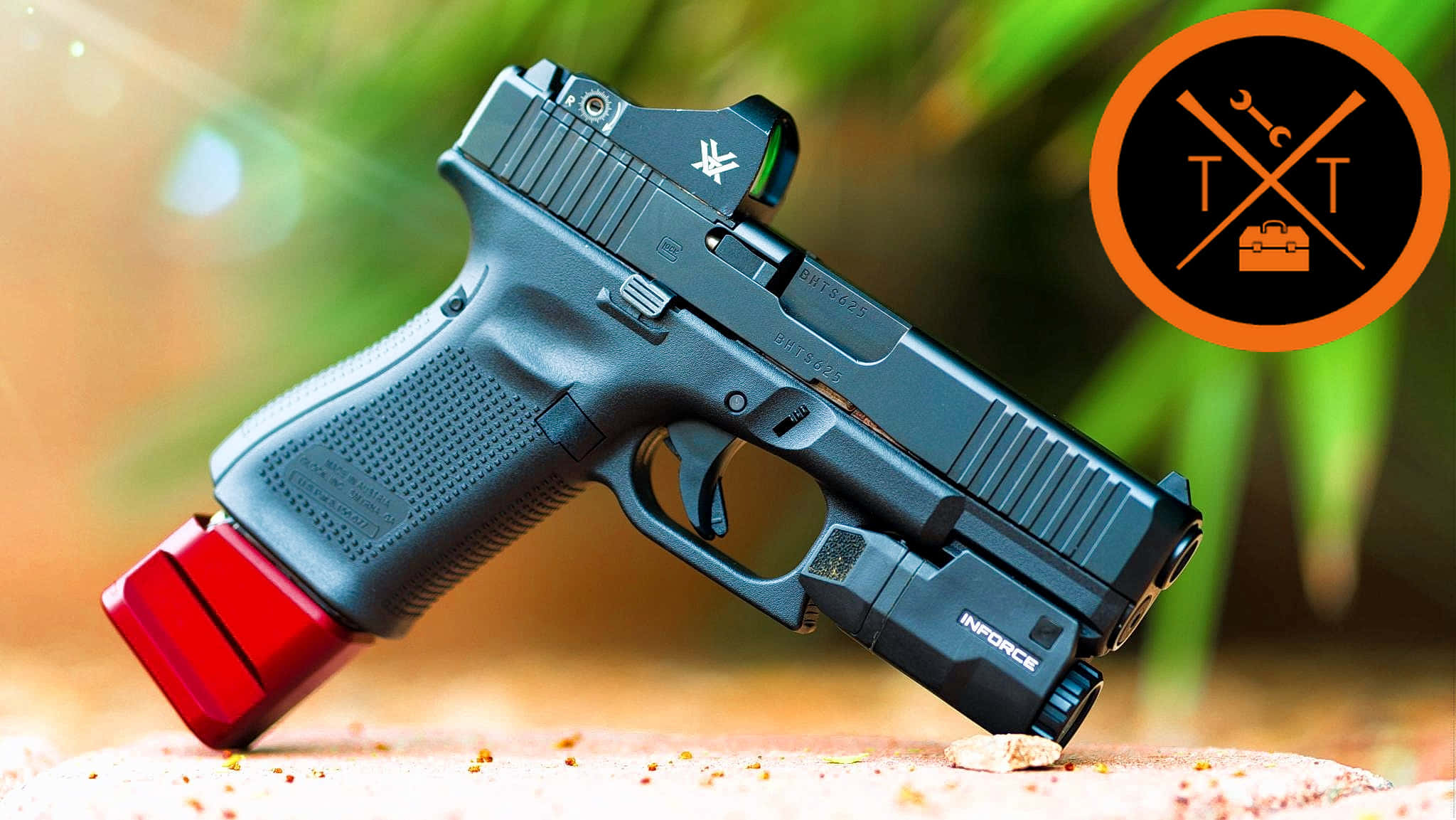 Glock 19 手槍 壁紙 — 一枝黑色手槍配紅色彈匣及戰術燈，擱在沙地上，背景是模糊的綠色樹葉。