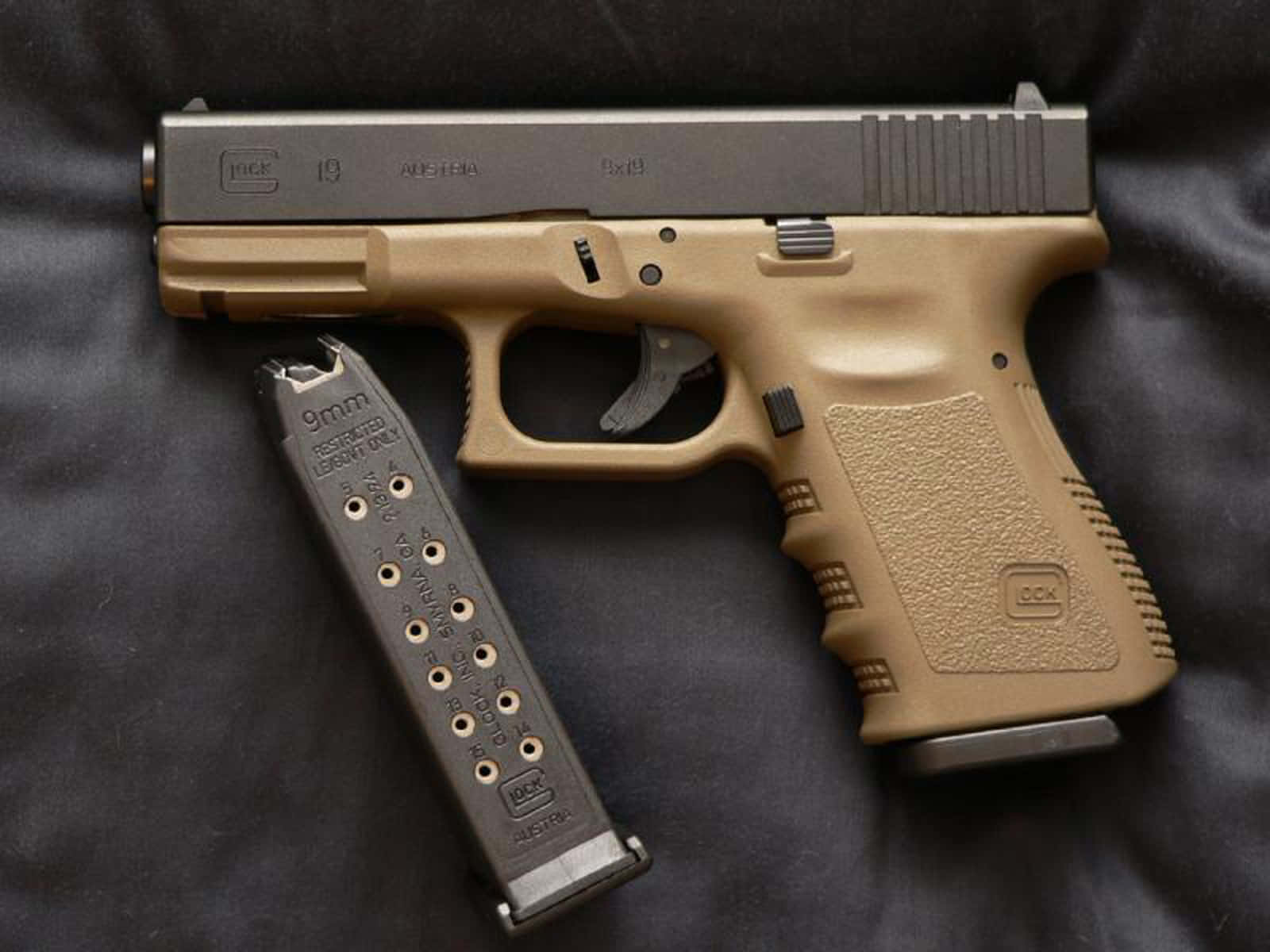 Glock 19 的強大威力 壁紙 — 一支沙色和黑色的 Glock 19 手槍連同 9mm 彈匣放在深色布料表面上。