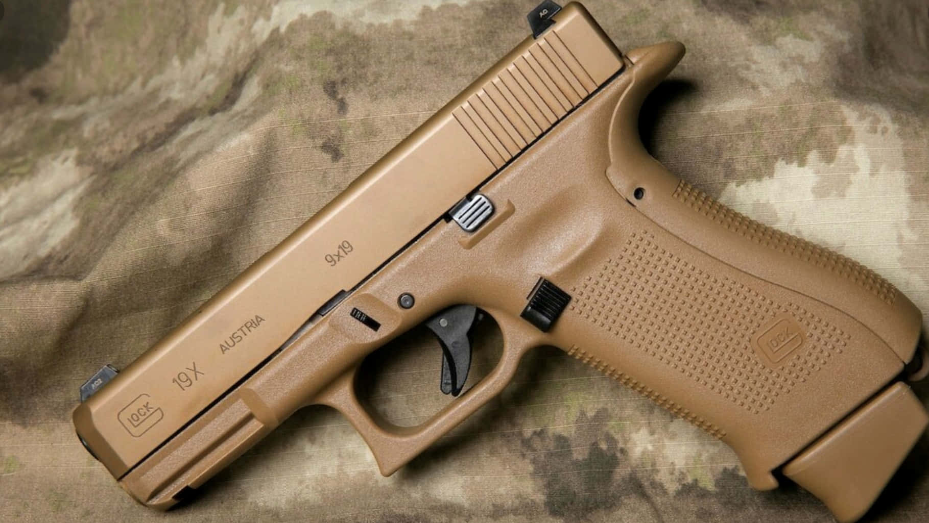 Glock 19 紧湊型 9mm 手槍 —— 強大於小體積 壁紙 — 一支沙色Glock 19X手槍放在帶有細緻紋理和雕刻標記的迷彩布料上。