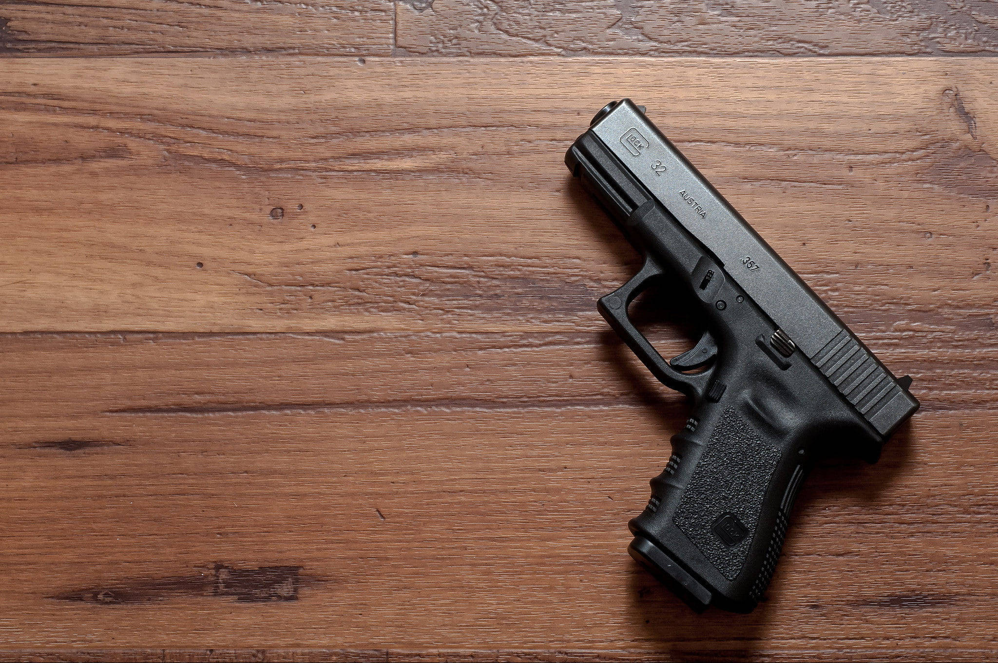 Glock 32 置於木桌 壁紙 — 一把黑色半自動手槍放在暖色調的木地板上，木紋和節疤清晰可見。