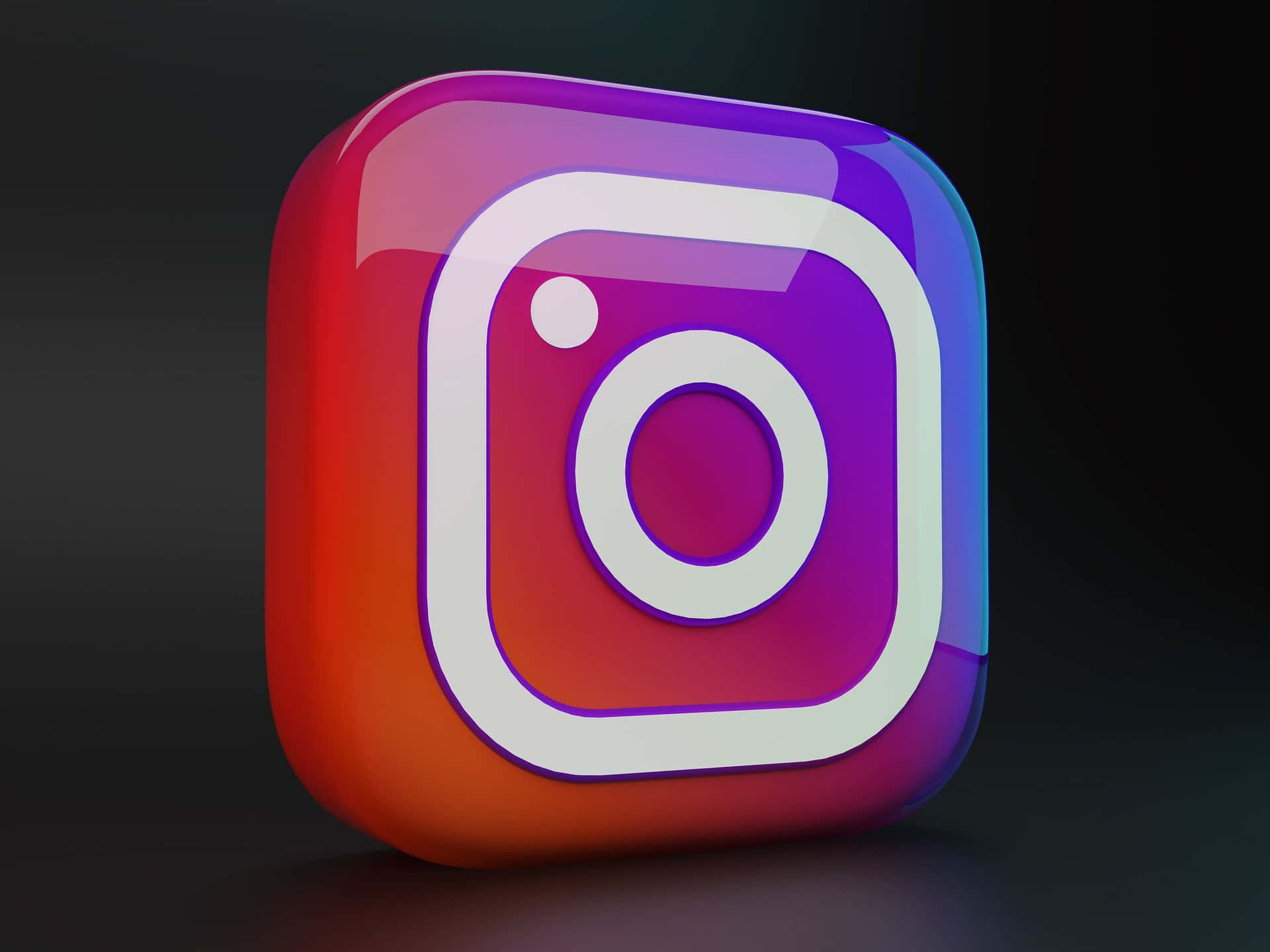  壁紙 — 一個帶有鮮豔漸變色彩的光澤3D渲染Instagram標誌圖標，置於深色背景上。