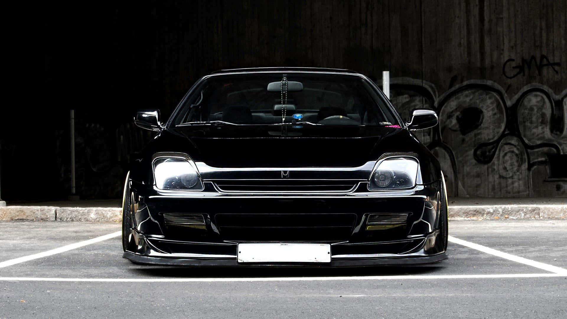Honda Prelude 桌布 壁紙 — 一輛光澤黑色改裝跑車，帶有定制保險槓和降低的姿態，夜間停在一個塗鴉覆蓋的城市地塊中。