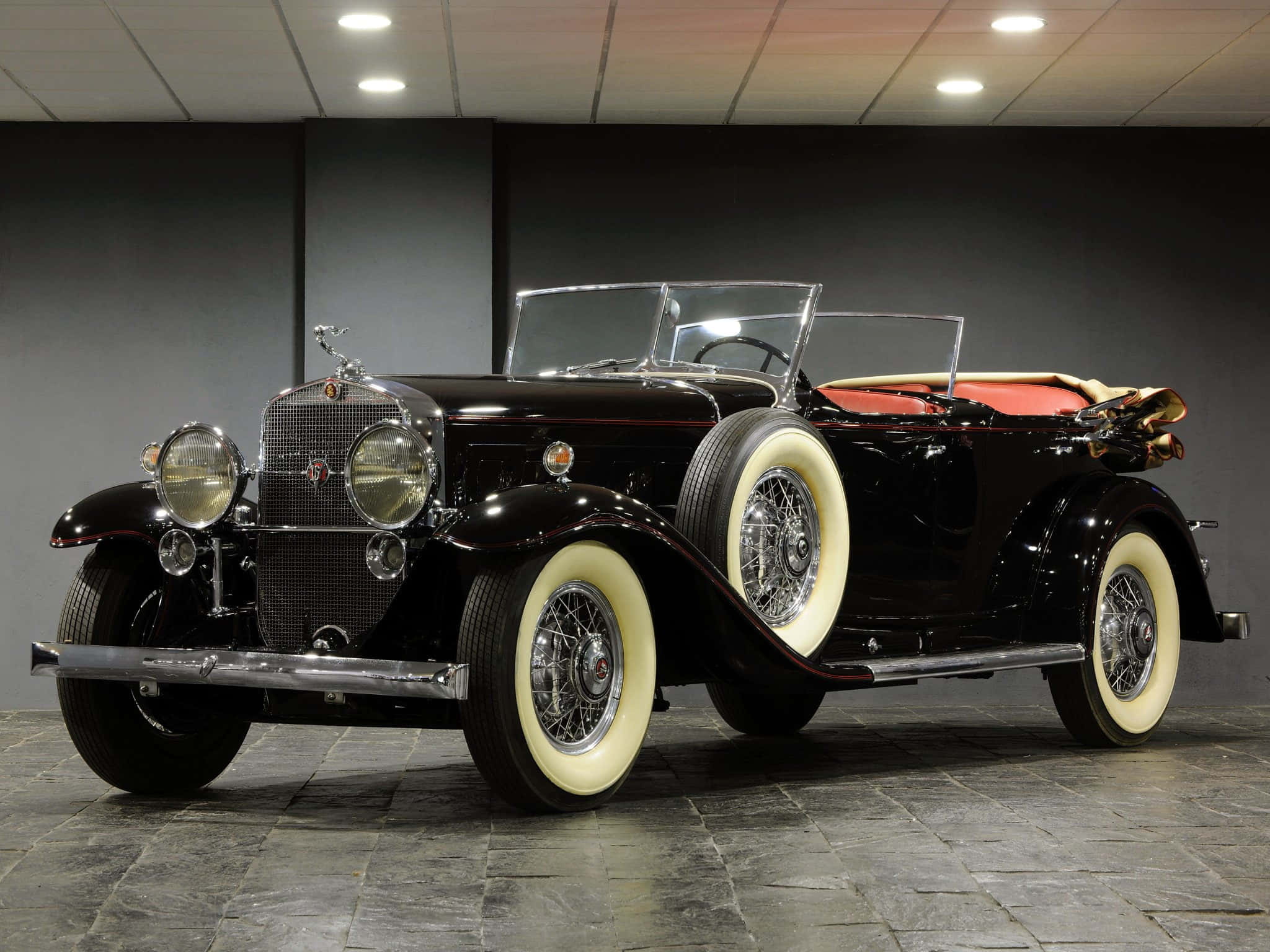 Cadillac Fleetwood 桌布 壁紙 — 一架光澤黑色復古開篷車，配以奶油色白邊輪胎和紅色內飾，優雅地停放在時尚的室內陳列室中。