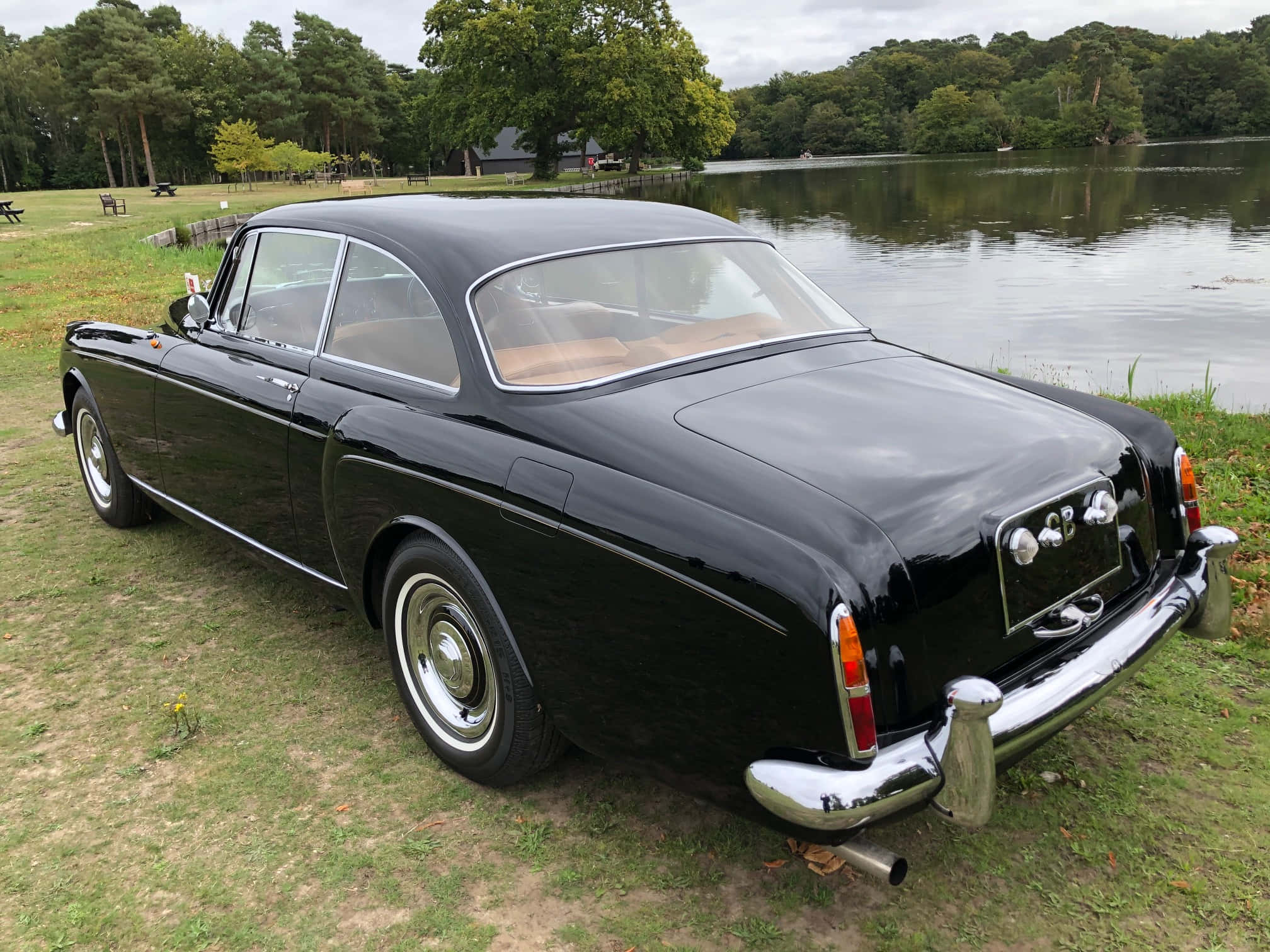Bentley S2 桌布 壁紙 — 一輛光澤黑色復古跑車停在草地上，旁邊是被樹木環繞的平靜湖泊。