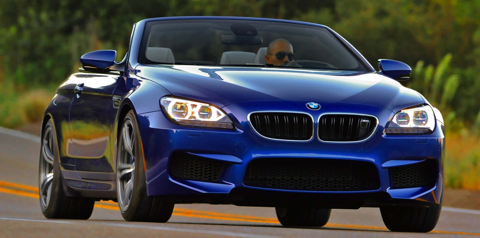 Bmw M6 桌布 壁紙 — 一架閃亮藍色BMW M6開篷跑車在陽光明媚的道路上疾馳，司機戴著太陽眼鏡。