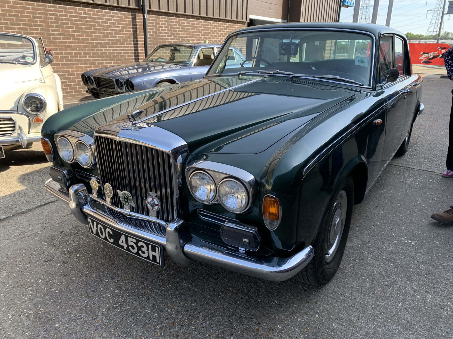 Bentley T1 桌布 壁紙 — 一輛光澤深綠色復古賓利S3轎車在明亮的日光下閃閃發光，停泊在瀝青停車場上其他經典汽車旁邊。