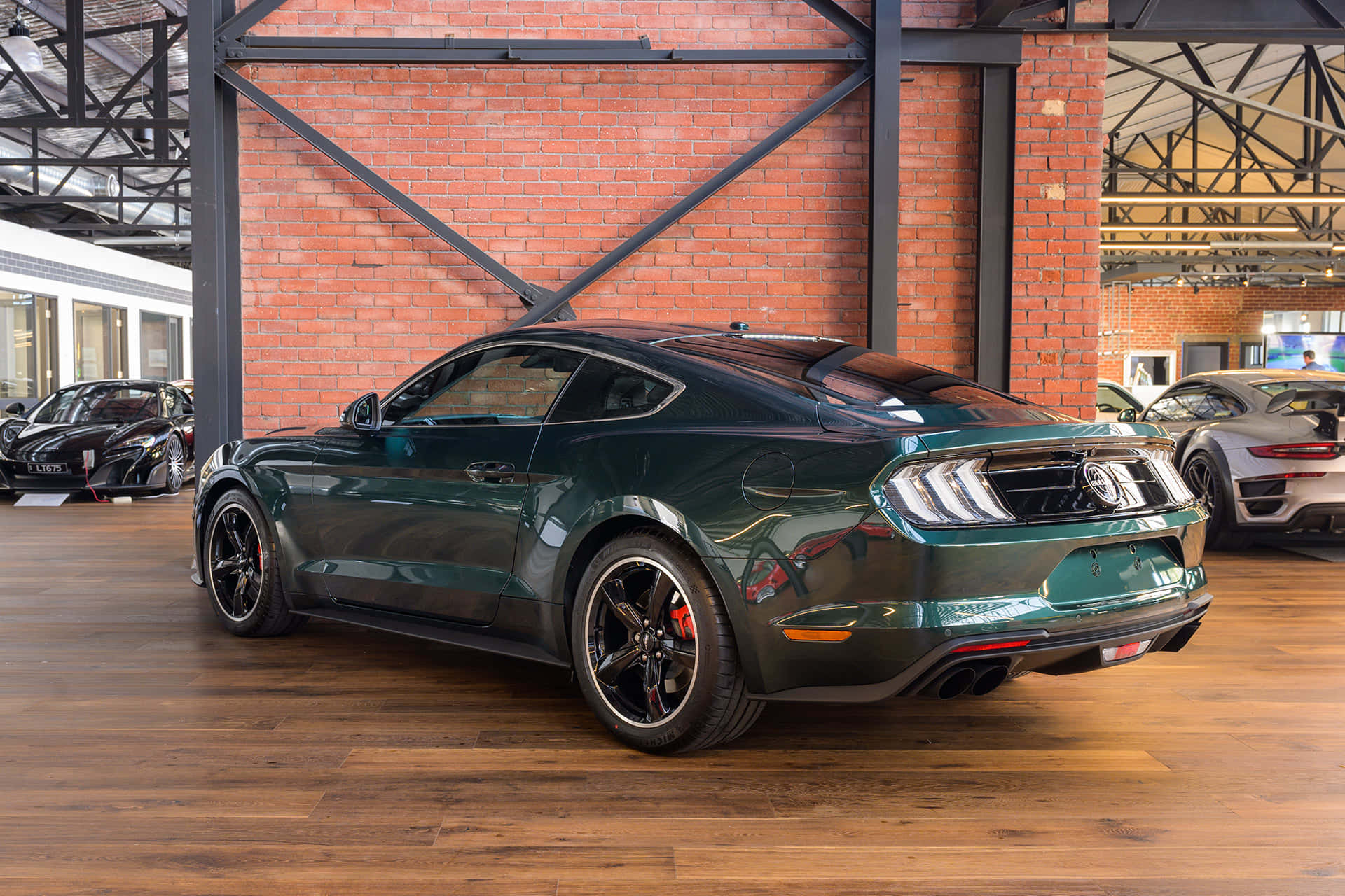 Ford Mustang Bullitt 桌布 壁紙 — 一輛光澤的綠色福特野馬雙門跑車停在室內木地板上，背景是帶有裸露鋼樑的紅磚牆。