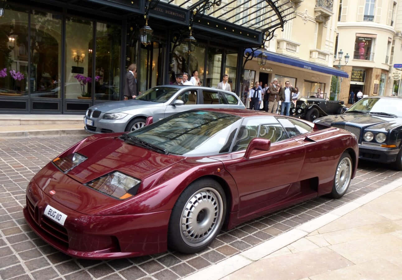 Bugatti Eb110 桌布 壁紙 — 一輛光澤的栗色布加迪EB110超級跑車停在鵝卵石街道上，前方是豪華精品店，有旁觀者。