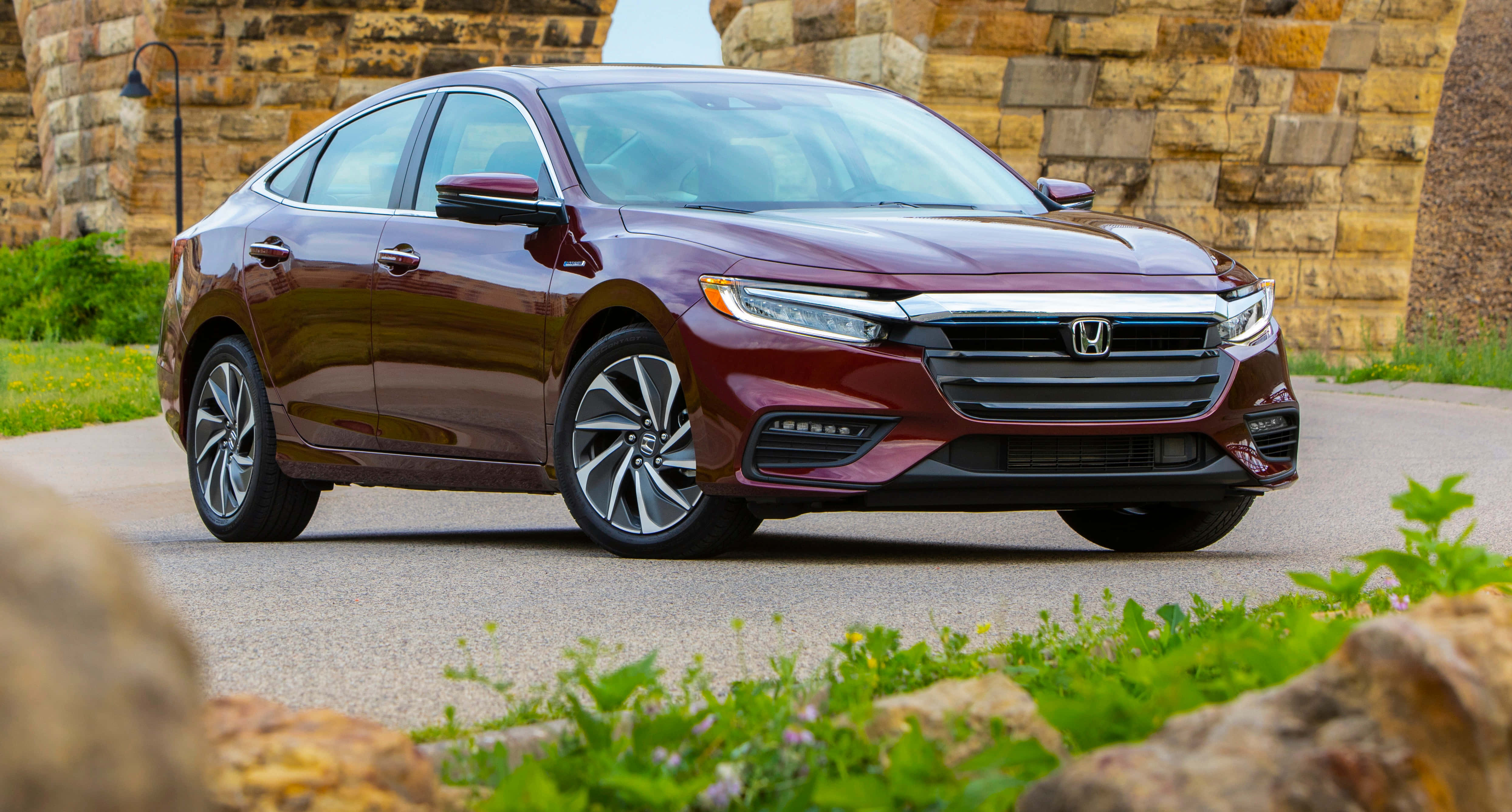 Honda Insight 桌布 壁紙 — 一輛光澤的栗色本田轎車停在石徑上，旁邊是質樸的石拱門，前景有綠植。