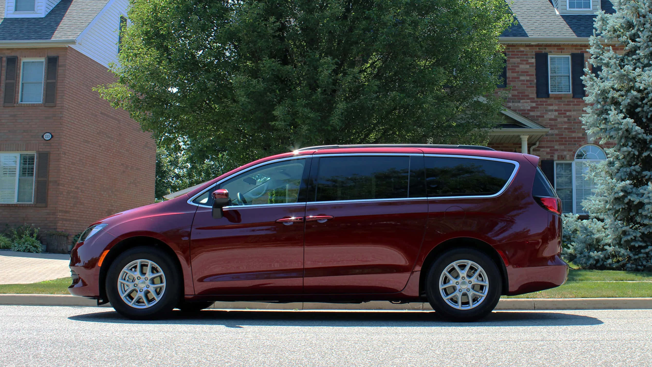 Chrysler Voyager 桌布 壁紙 — 一輛光澤的栗色小型貨車停泊在郊區街道上，旁邊是磚房和綠樹，在明亮的日光下。