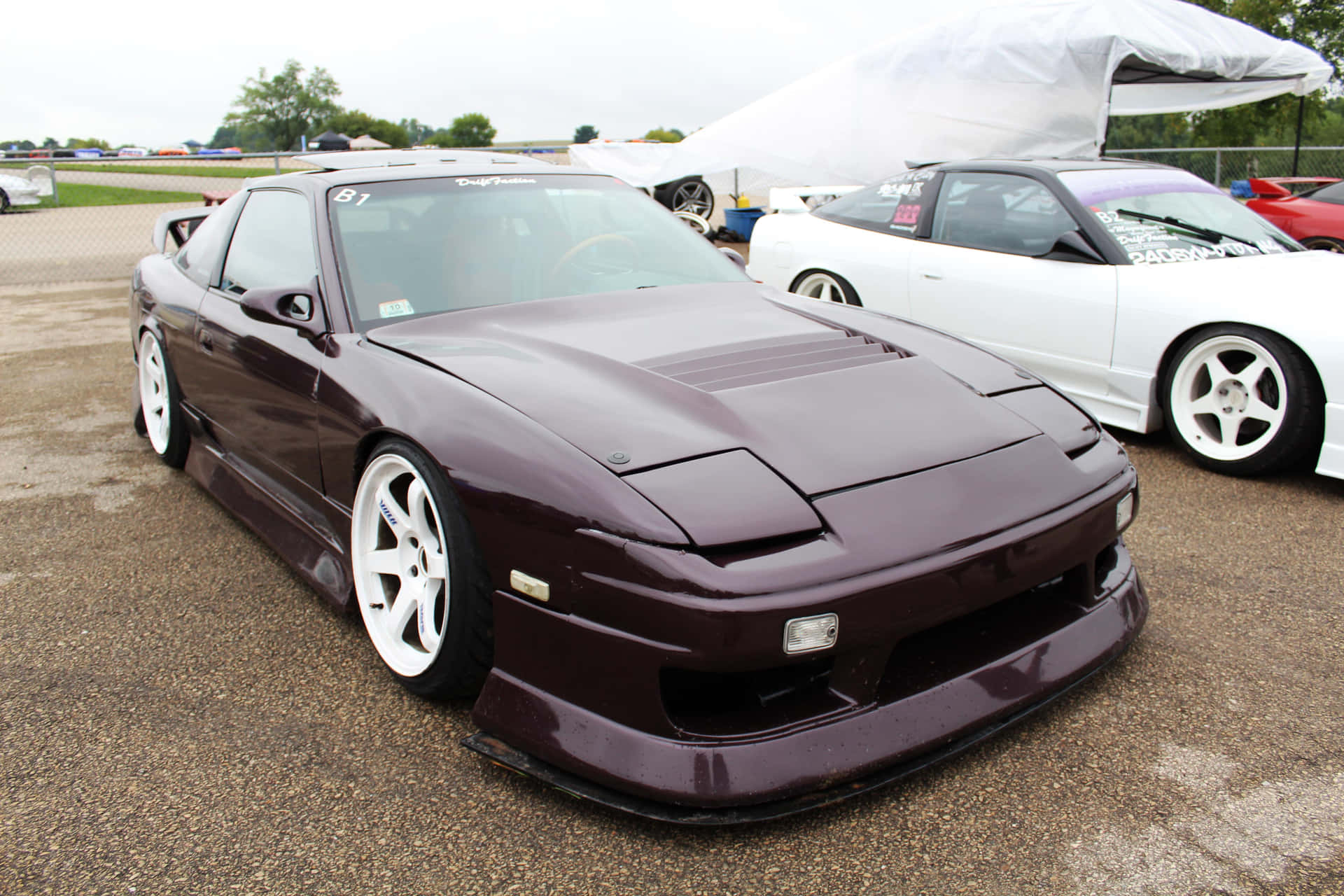  壁紙 — 一架亮面栗色日產S14跑車配白色輪圈，在陰天停泊於戶外車展。