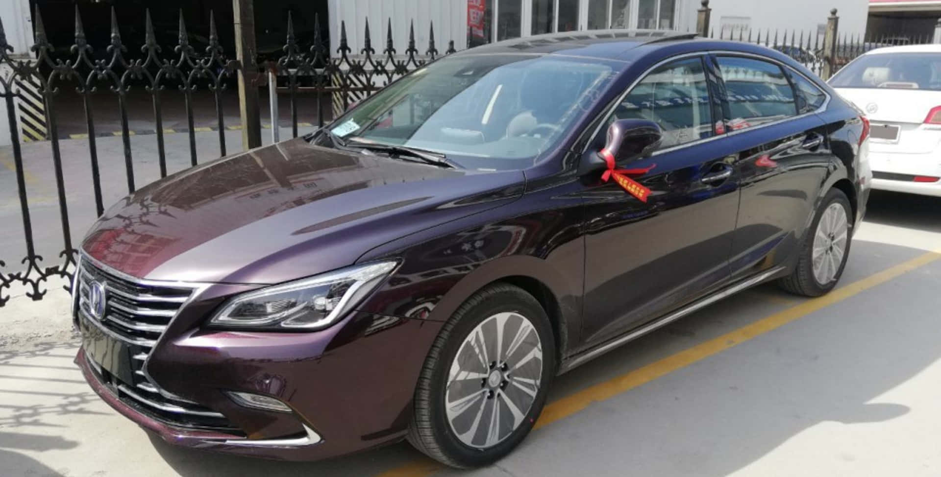  壁紙 — 一輛亮面栗色轎車停放在戶外，側鏡上繫著紅色絲帶。