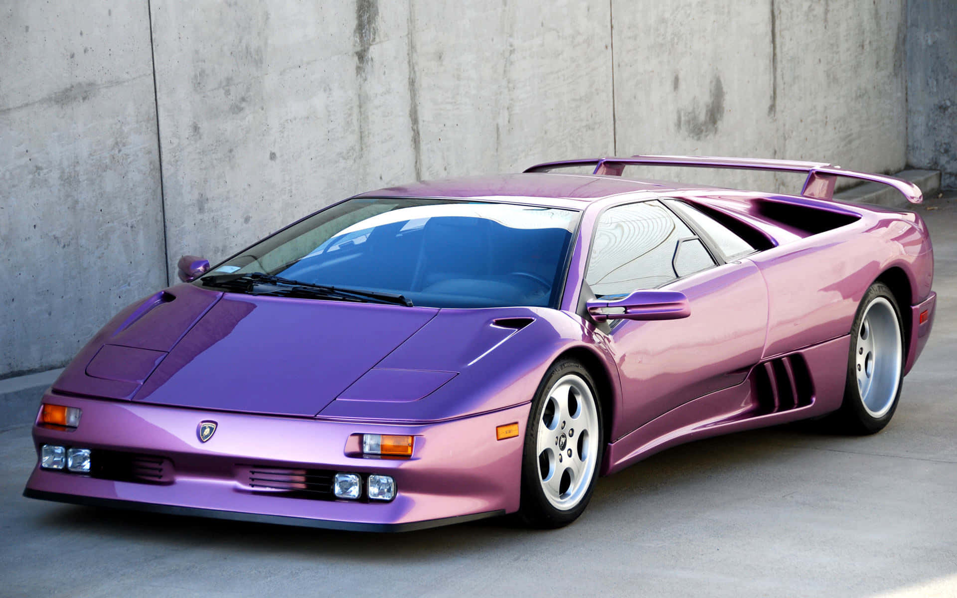 Lamborghini Diablo 桌布 壁紙 — 一輛光澤紫色林寶堅尼 Diablo 跑車在明亮日光下停泊在混凝土牆旁。