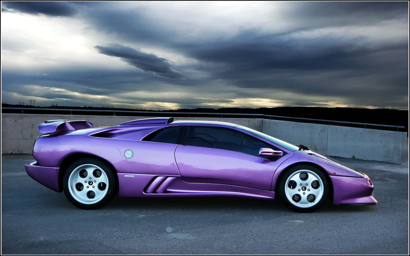 Lamborghini Diablo 桌布 壁紙 — 一架光澤的紫色林寶堅尼Diablo跑車停泊在天橋上，背景是黃昏時分戲劇性的暴風雨天空。